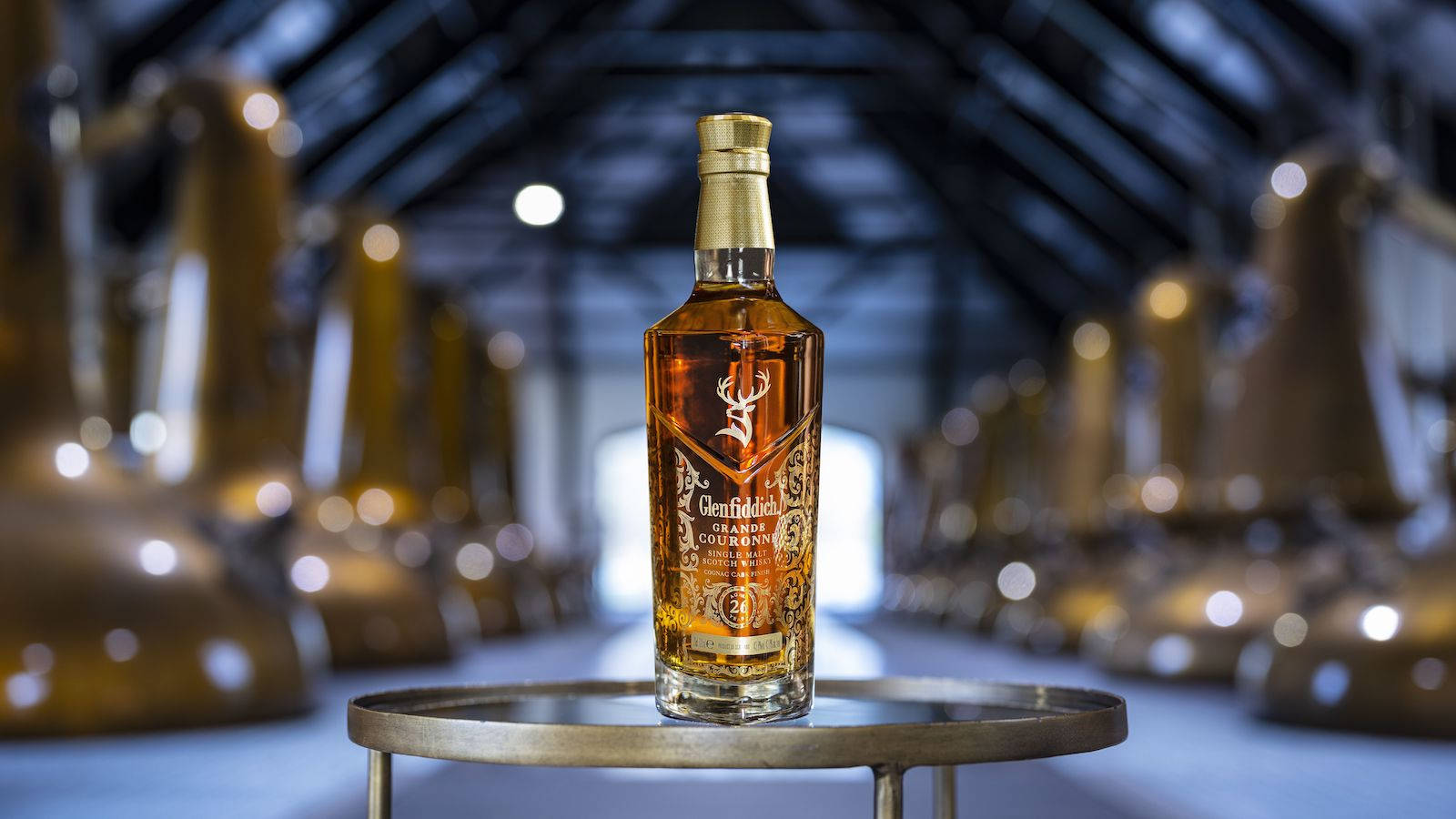 alcohol 桌布 壁紙 — 一瓶 Glenfiddich 威士忌在蒸餾廠的黃銅架上，在模糊的銅製蒸餾器中閃耀。