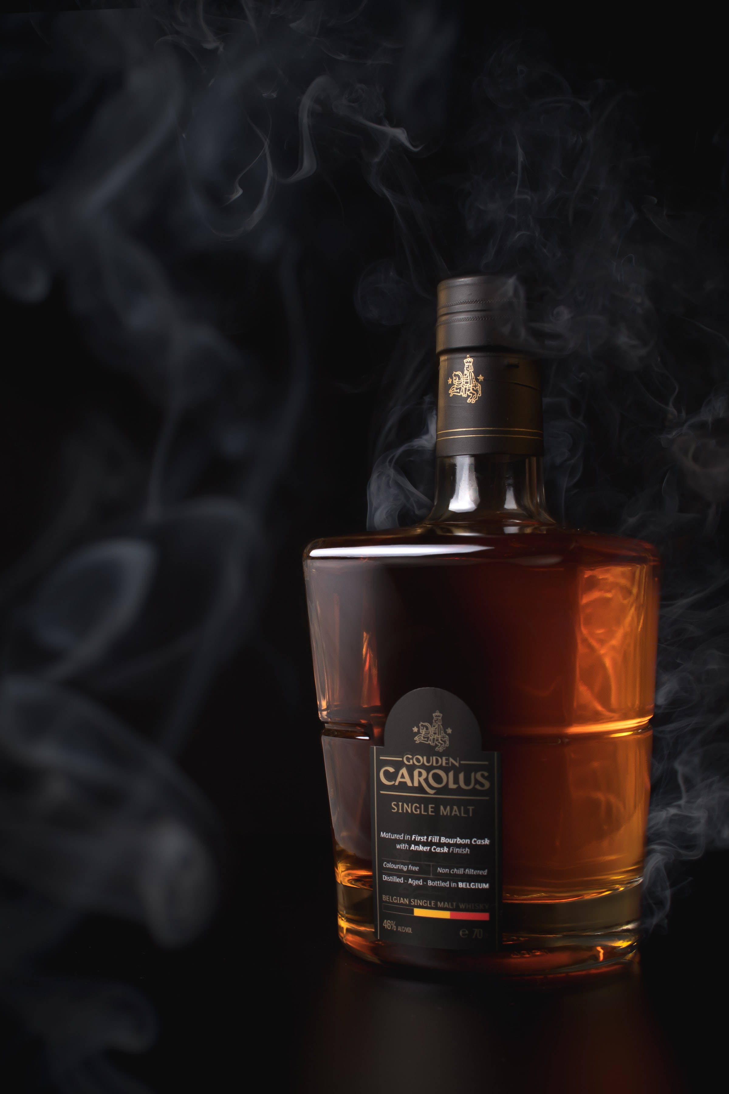 alcohol 桌布 壁紙 — 一瓶 Golden Carolus 單一麥芽威士忌在黑色背景下溫暖地發光，煙霧在它周圍繚繞。