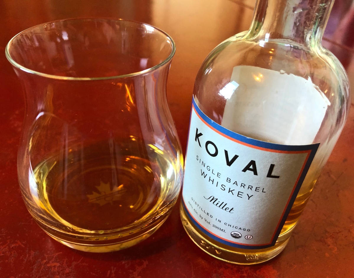 drinks 桌布 壁紙 — 一瓶 Koval Millet 單桶威士忌放在溫暖的紅色表面上，旁邊有一個裝著琥珀色液體的玻璃杯。