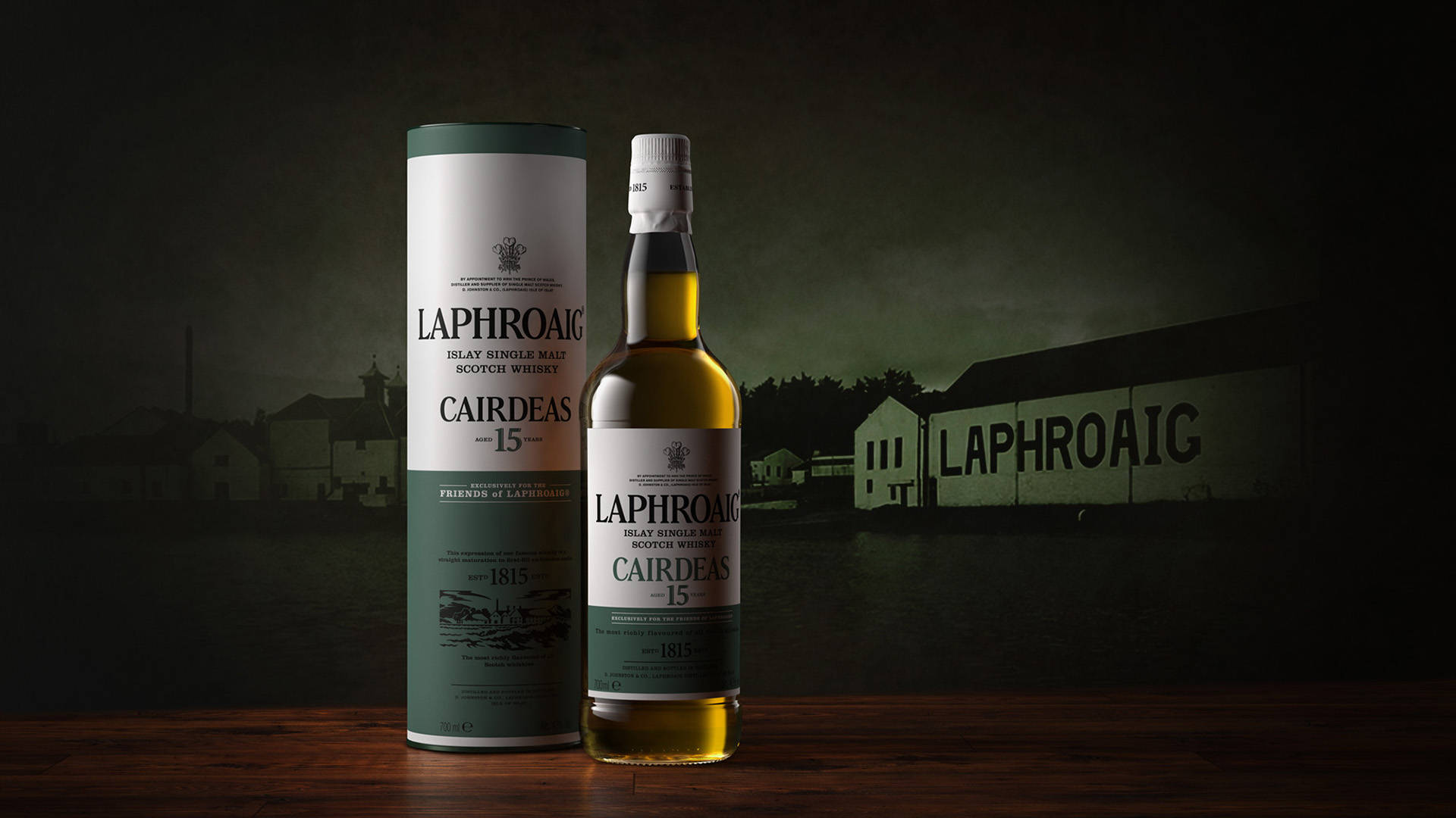 iPhone 桌布 壁紙 — 一瓶 Laphroaig Cairdeas 15 年威士忌和其管狀包裝在木質表面上溫暖地發光，背景是陰暗、富有氣氛的蒸餾廠。