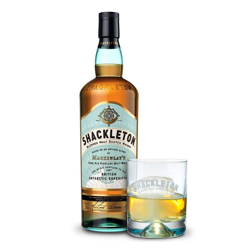 Drink 桌布 壁紙 — 一瓶 Shackleton Blended Malt Scotch Whisky 放在一個裝滿琥珀色液體和冰塊的玻璃杯旁邊，背景是潔淨的白色。