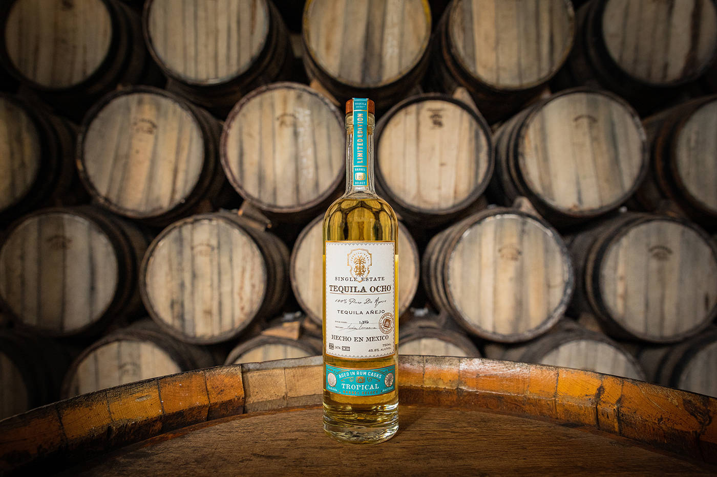 bottle 桌布 壁紙 — 一瓶 Single Estate Tequila Ocho 放在木桶上，背景是一排排陳年的木桶。