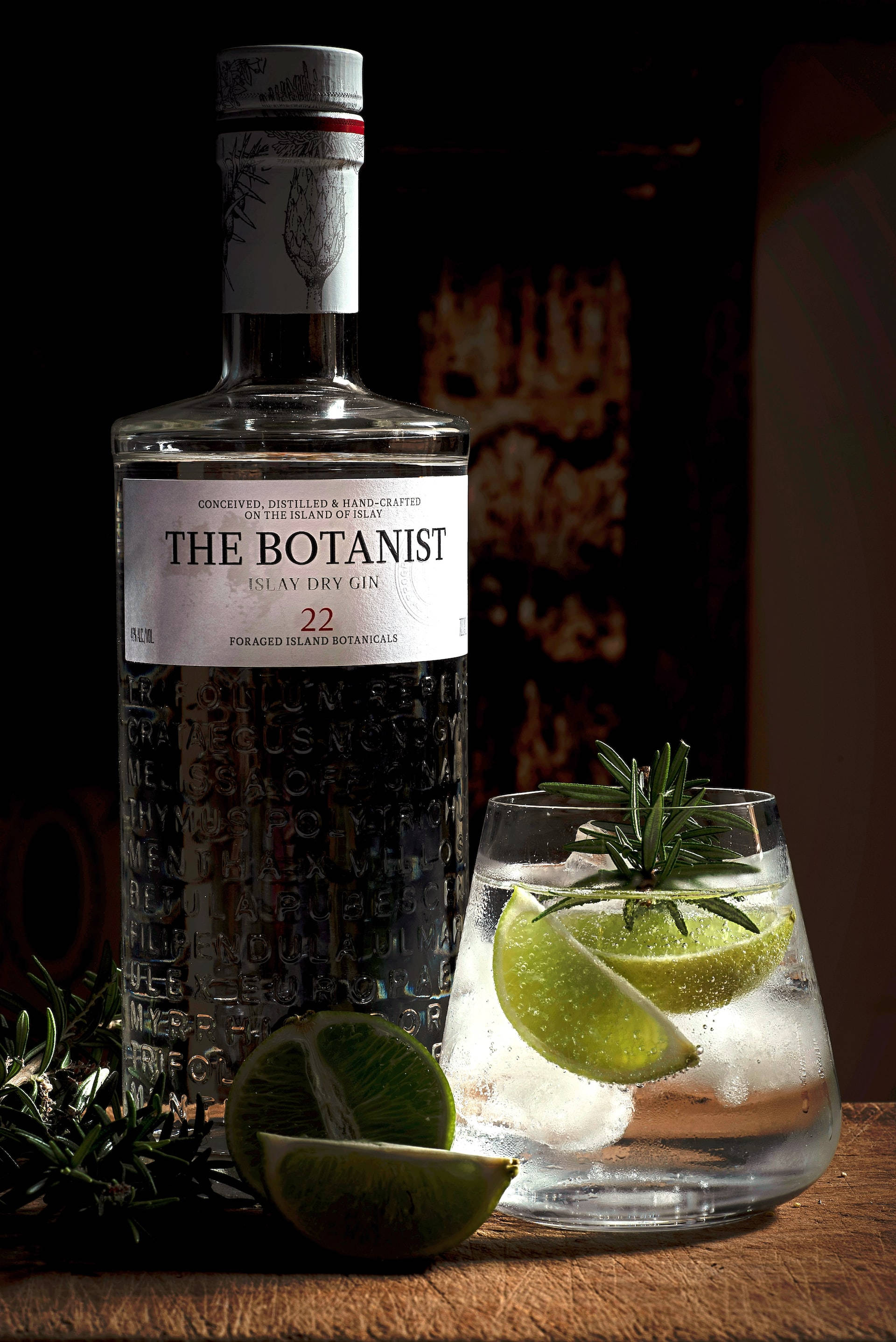 drinks 桌布 壁紙 — 一瓶 The Botanist 琴酒放在木桌上，旁邊有一杯加了萊姆、迷迭香和冰塊的琴酒。