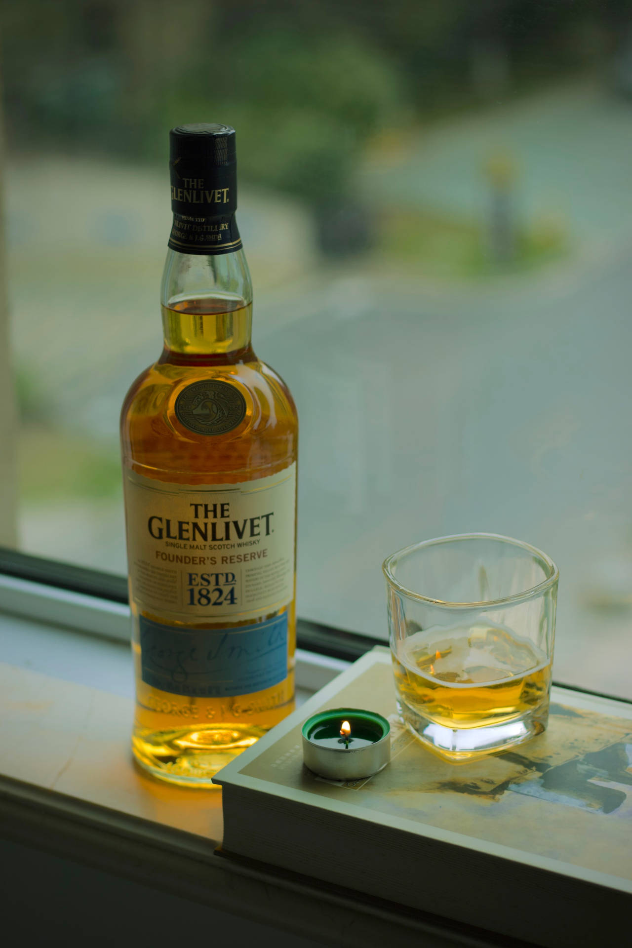 alcohol 桌布 壁紙 — 一瓶 The Glenlivet Founder's Reserve 威士忌和一杯加冰的威士忌放在窗台上，旁邊有一盞點燃的茶燭。