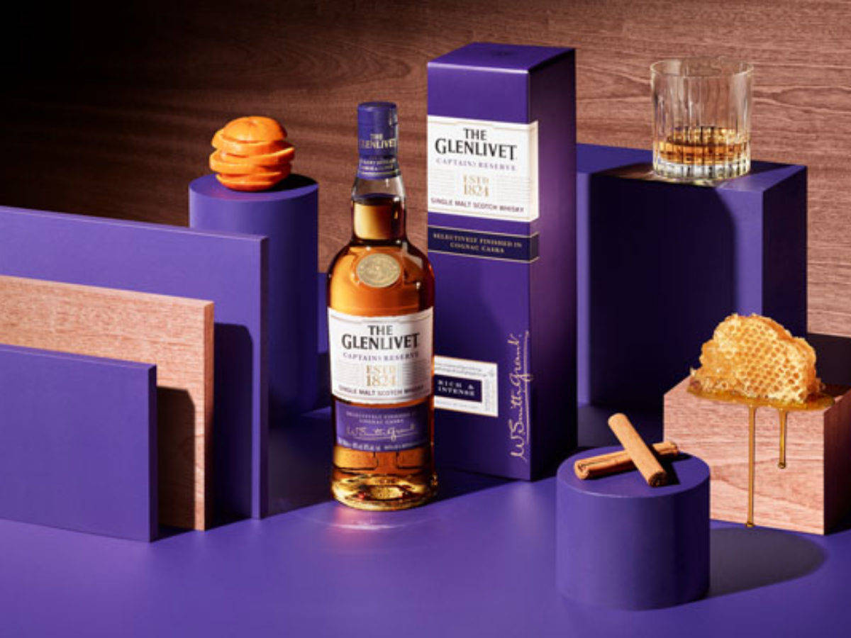 飲料 桌布 壁紙 — 一瓶 The Glenlivet 威士忌在充滿活力的紫色幾何套裝中居中，搭配蜂巢肉桂和一杯琥珀色液體。