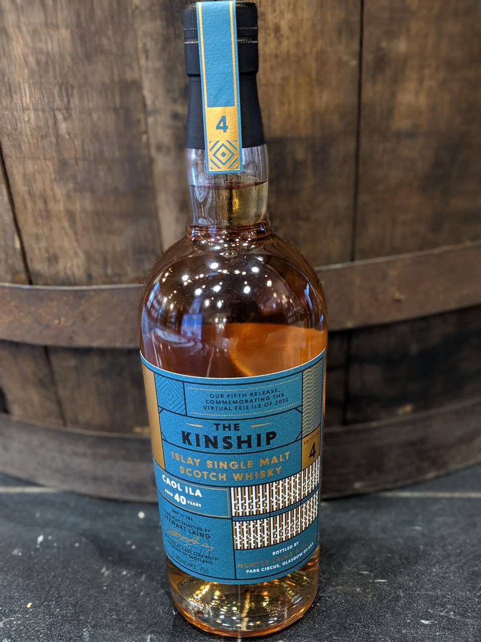 alcohol 桌布 壁紙 — 一瓶 The Kinship Islay 單一麥芽蘇格蘭威士忌靠在一個質樸的木桶上，裡面可見琥珀色的液體。