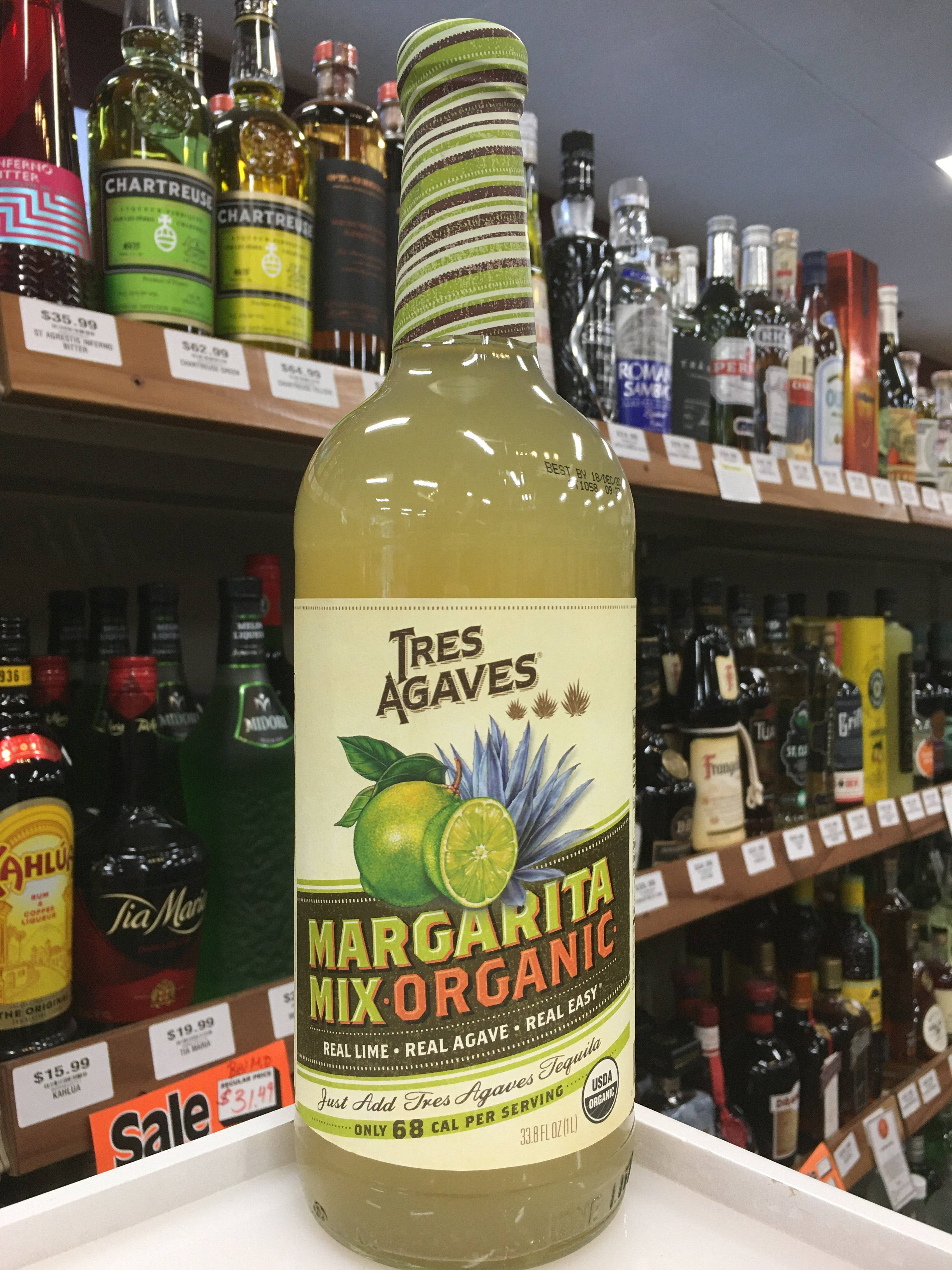 drinks 桌布 壁紙 — 一瓶 Tres Agaves Margarita Mix Organic 在明亮的螢光燈下，顯眼地放置在商店貨架上，周圍環繞著其他酒瓶。