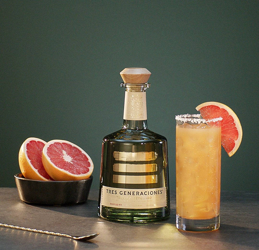 cocktail 桌布 壁紙 — 一瓶 Tres Generaciones 龍舌蘭酒放在一張深色桌子上，旁邊有一杯柑橘雞尾酒和半個葡萄柚，背景是柔和的綠色牆壁。