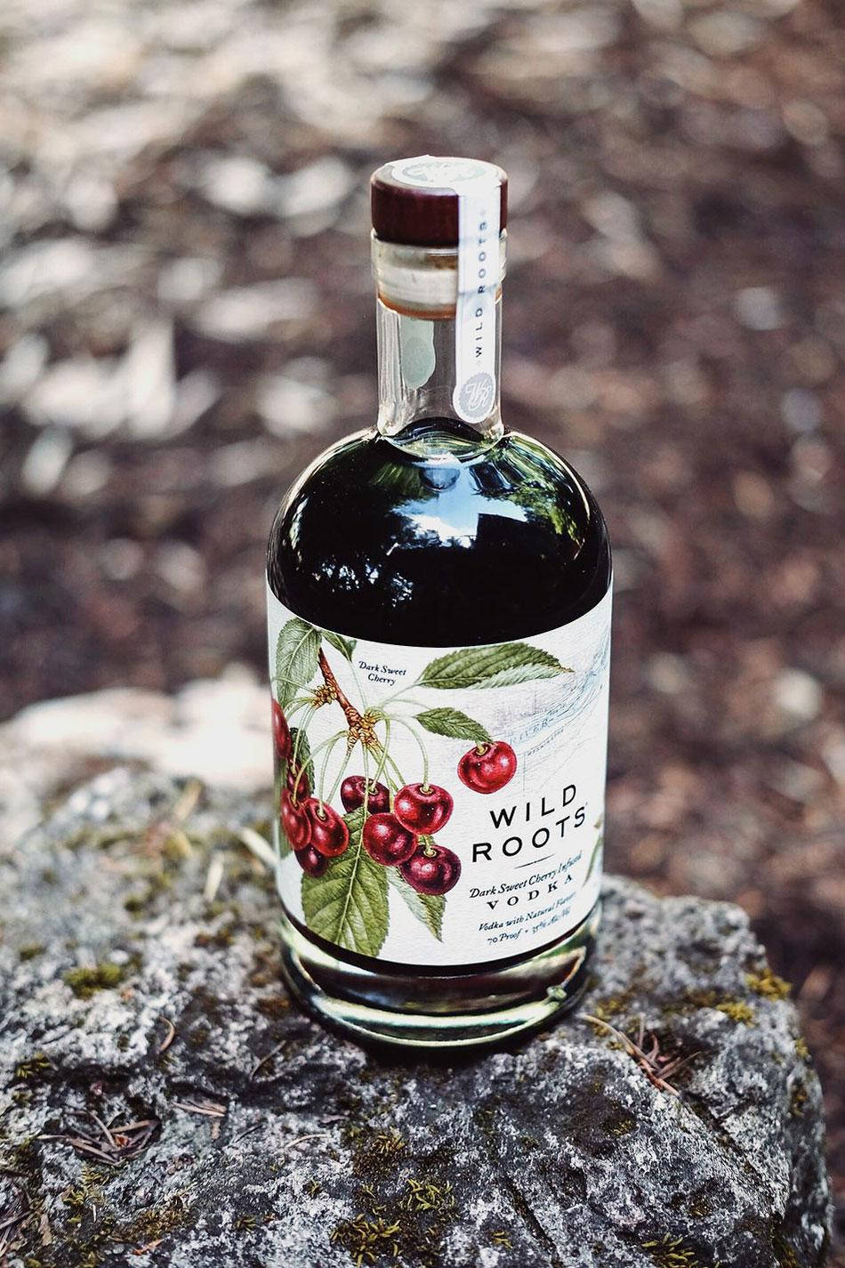 bottle 桌布 壁紙 — 一瓶 Wild Roots 深色甜櫻桃伏特加酒放在森林環境中的一塊長滿苔蘚的石頭上。
