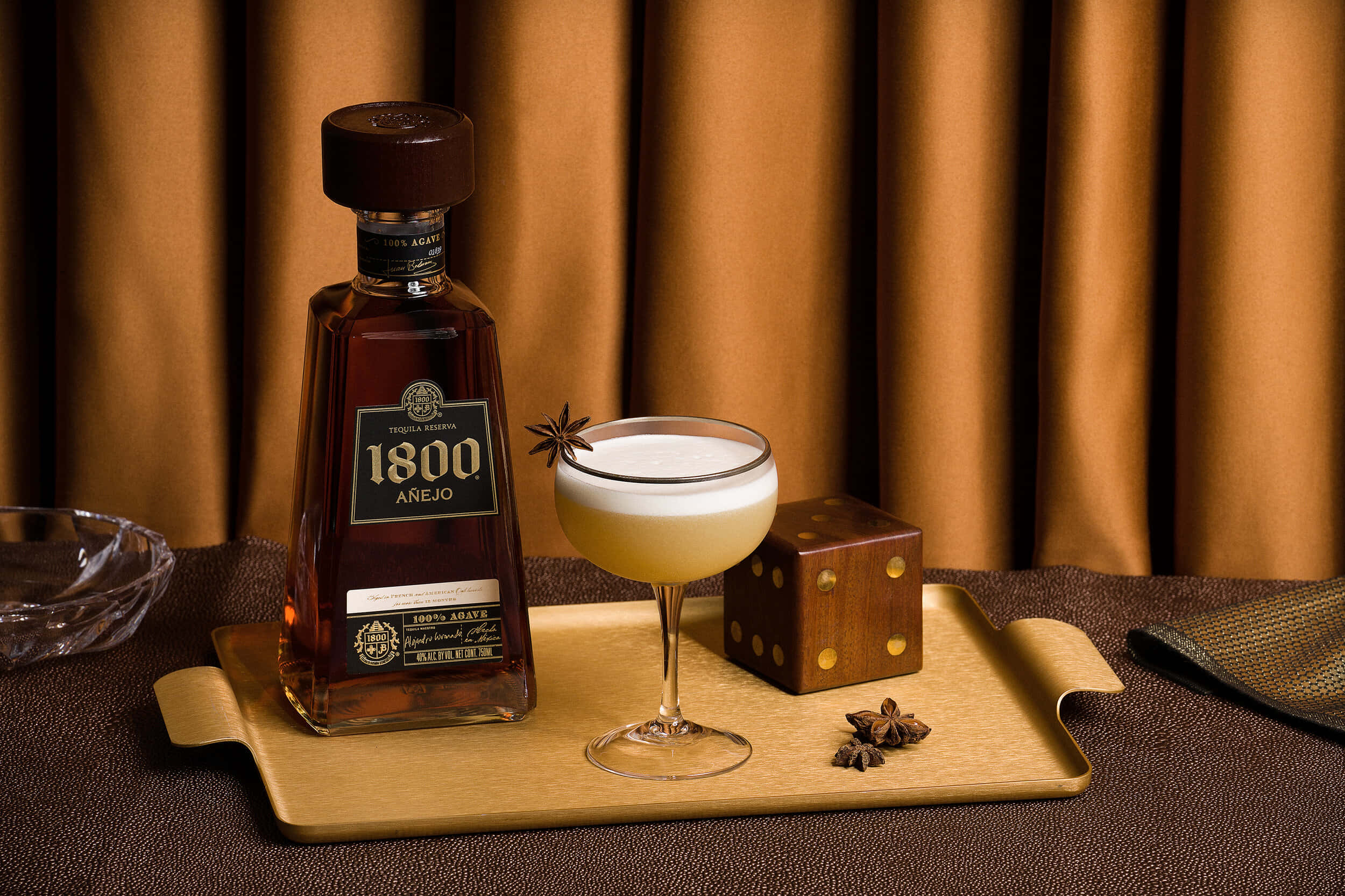 alcohol 桌布 壁紙 — 一瓶1800 Añejo龍舌蘭酒和一杯以八角裝飾的泡沫雞尾酒優雅地放在木托盤上，背景是溫暖的棕色窗簾。