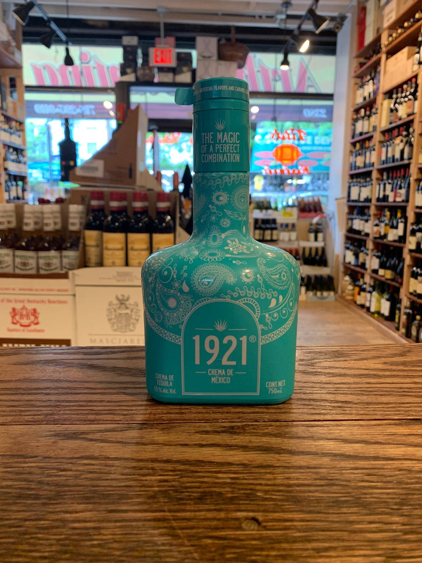 drinks 桌布 壁紙 — 一瓶1921 Crema de Mexico青綠色龍舌蘭酒，飾有華麗的白色圖案，放在溫暖燈光的酒舖的質樸木櫃檯中央。