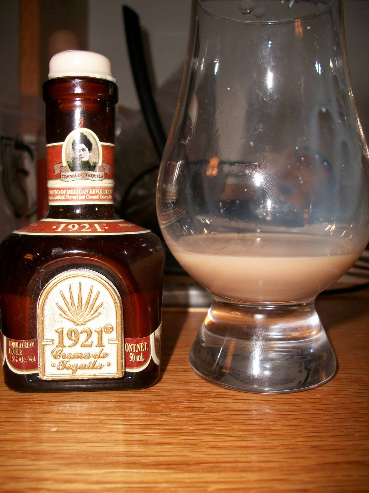 drinks 桌布 壁紙 — 一瓶1921 Tequila Cream Liqueur放在木製檯面上，旁邊有一個玻璃杯，裡面裝著其奶油色的液體。