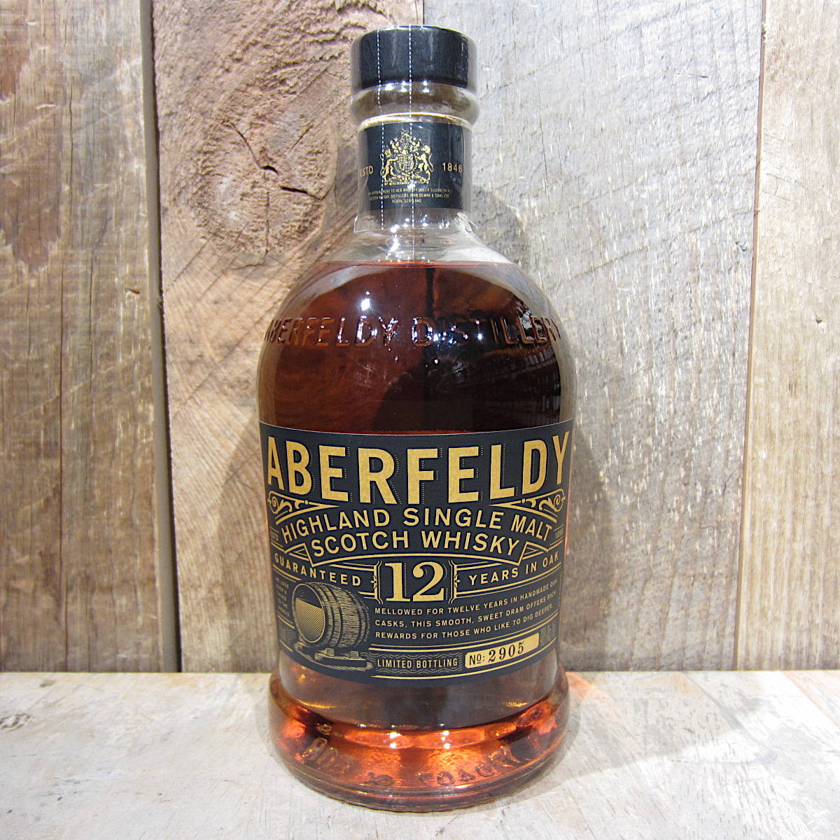 飲料 桌布 壁紙 — 一瓶Aberfeldy 12年高地單一麥芽蘇格蘭威士忌，以質樸的木質背景襯托，內部可見溫暖的琥珀色液體。