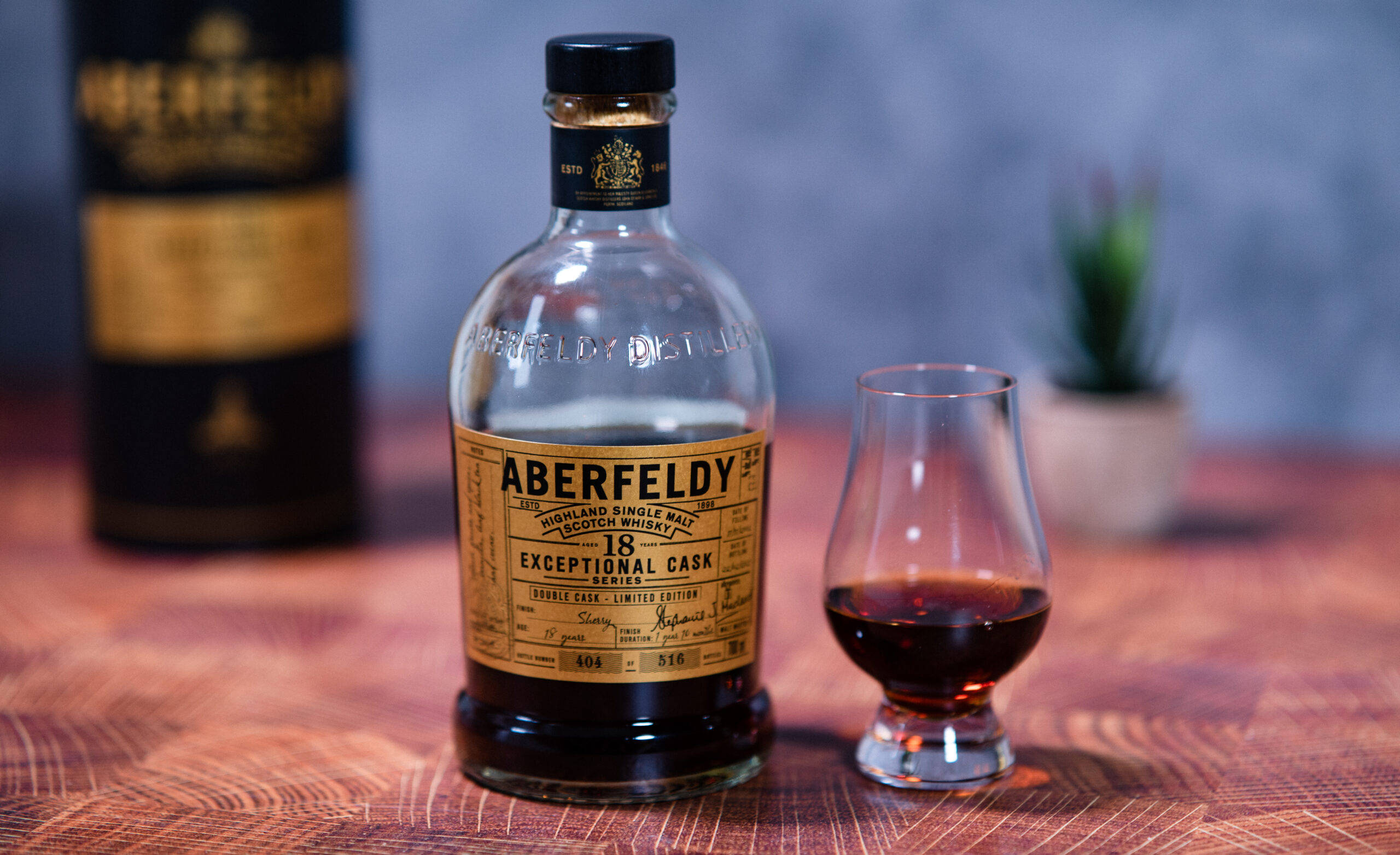 Drink 桌布 壁紙 — 一瓶Aberfeldy 18年單一麥芽威士忌放在木桌上，旁邊有一個裝滿琥珀色液體的品酒杯。