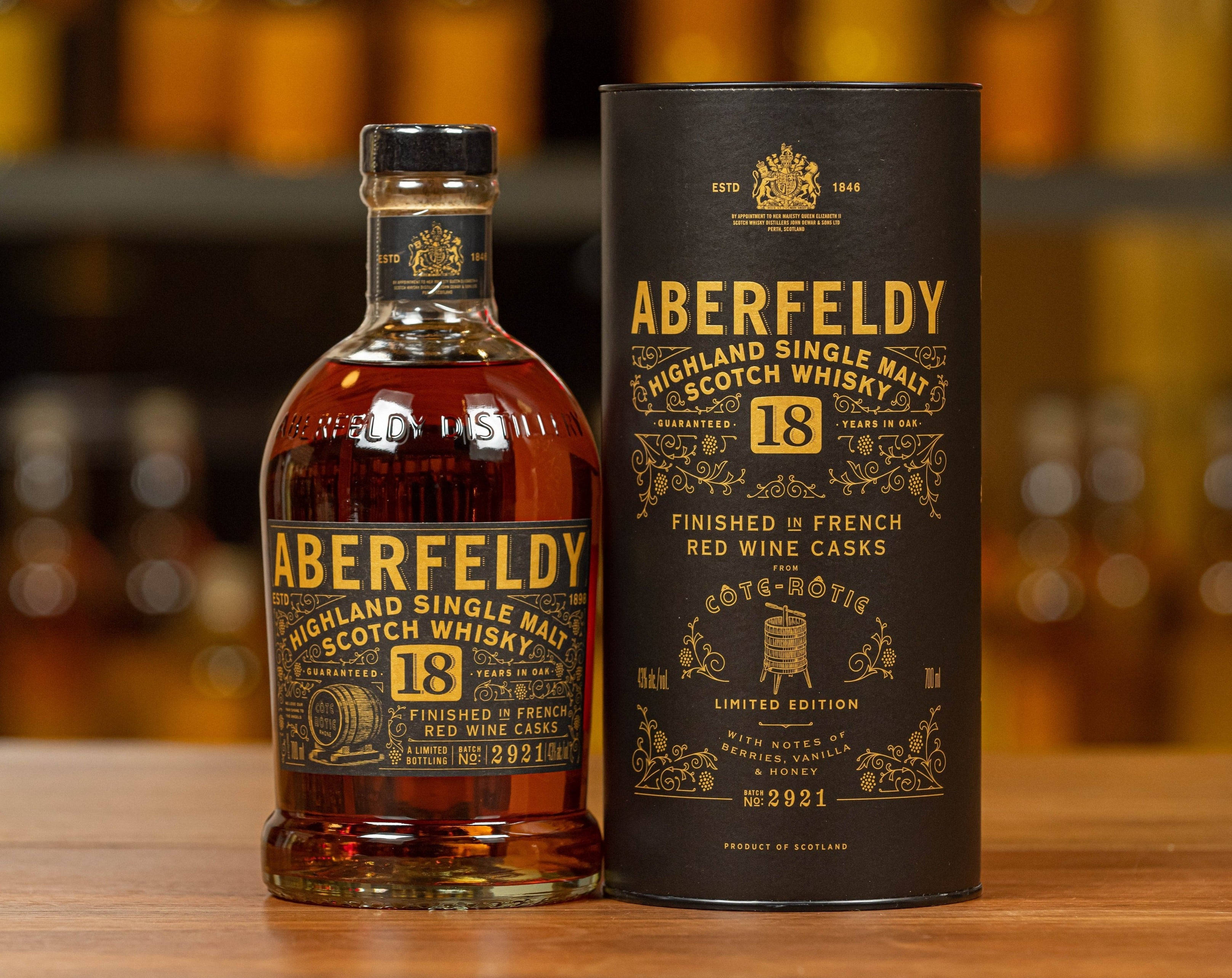 飲料 桌布 壁紙 — 一瓶Aberfeldy 18年高地單一麥芽蘇格蘭威士忌及其黑色管狀盒放在木質表面上，背景是模糊的琥珀色瓶子。