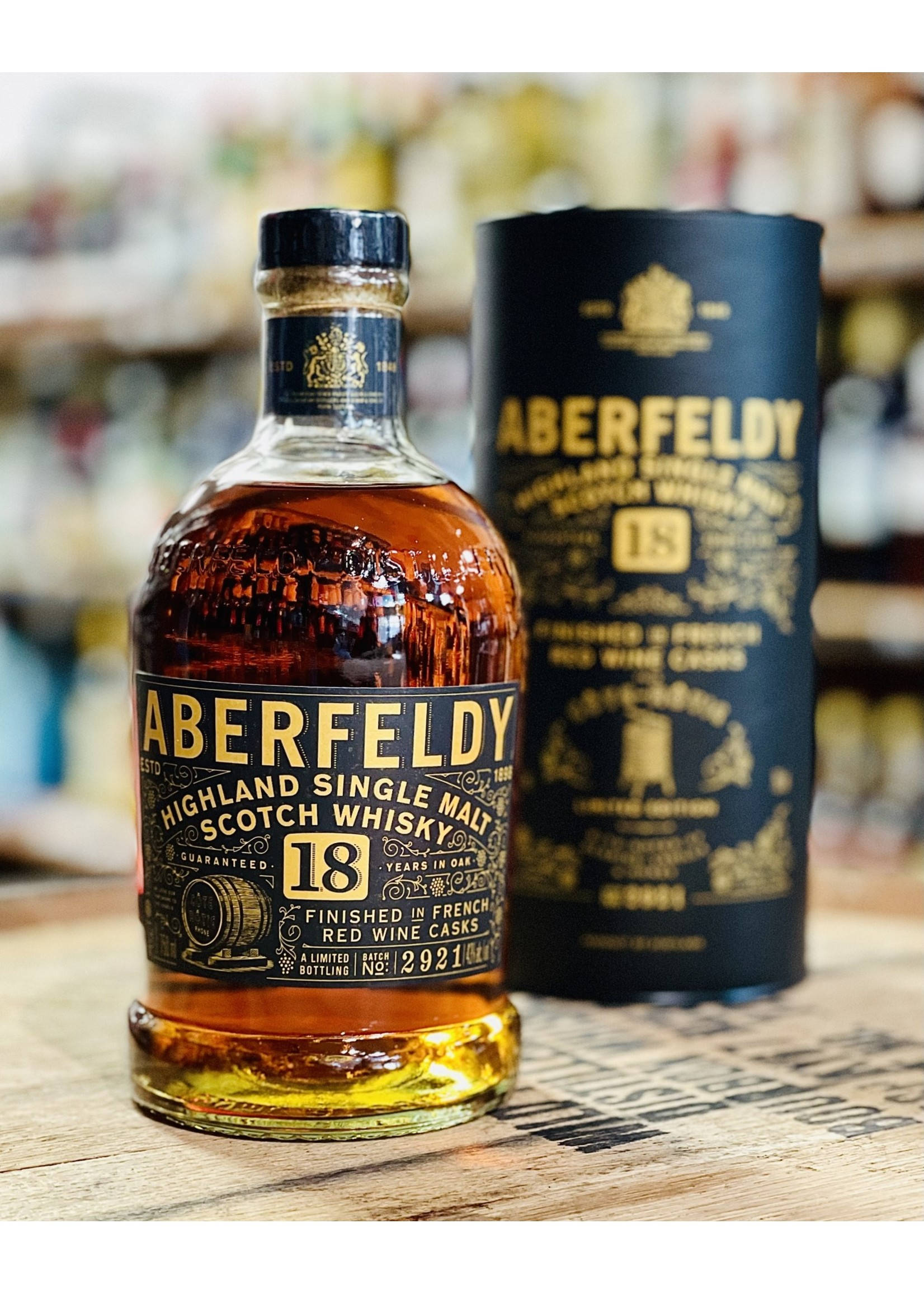 Drink 桌布 壁紙 — 一瓶Aberfeldy 18年高地單一麥芽蘇格蘭威士忌及其黑色管狀盒放在木質表面上，背景是模糊的酒類商店。