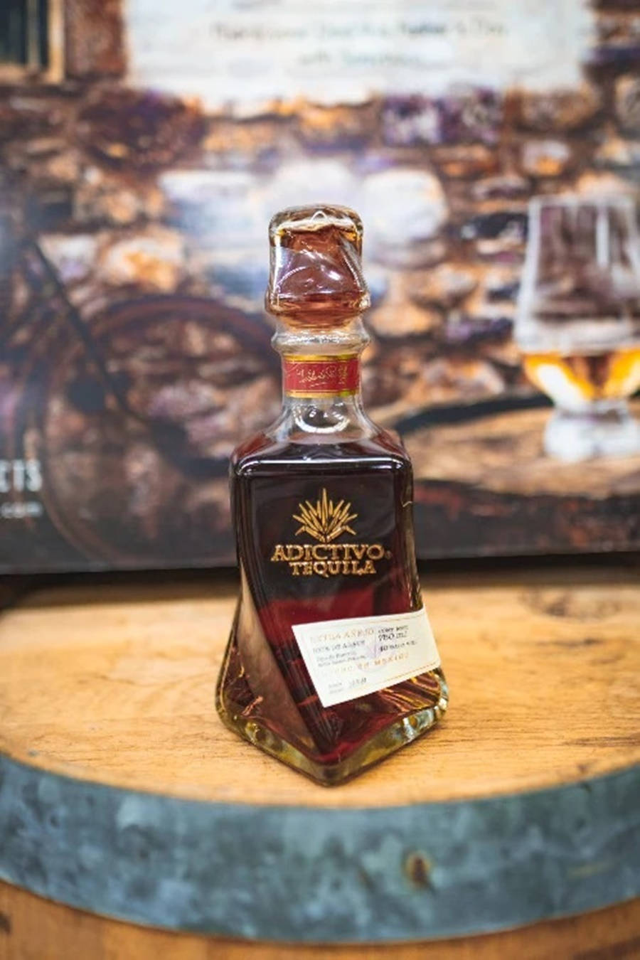 iPhone 桌布 壁紙 — 一瓶Adictivo Tequila放在木桶頂部，旁邊有玻璃杯和質樸的石牆背景。
