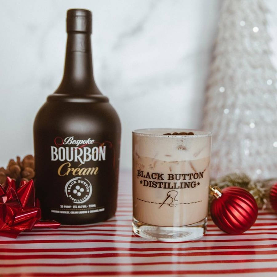 alcohol 桌布 壁紙 — 一瓶Black Button Bourbon Cream和一杯奶油雞尾酒放在紅色條紋桌布上，旁邊是節日紅色裝飾品和一棵白色聖誕樹。