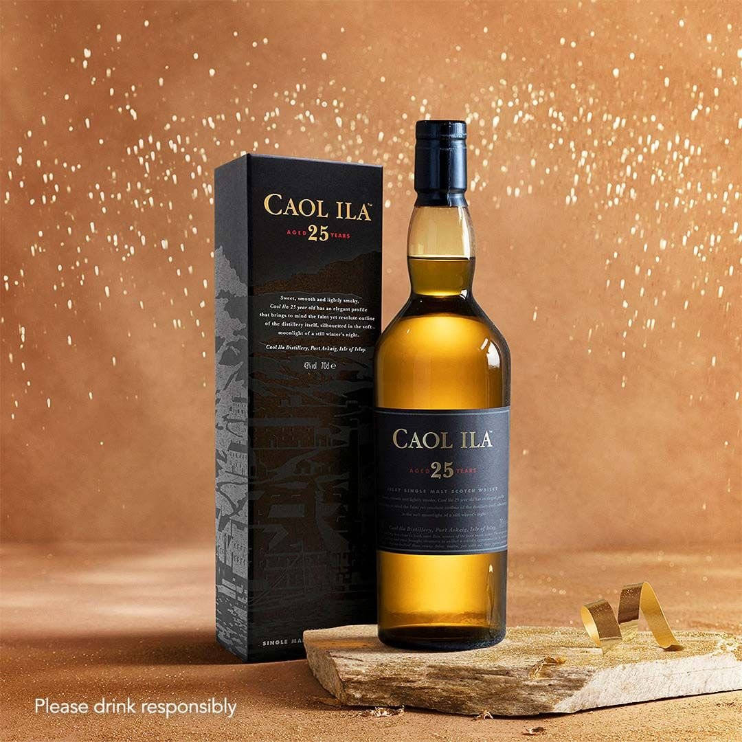 alcohol 桌布 壁紙 — 一瓶Caol Ila 25年威士忌連同其盒子放在一塊質樸的木板上，背景是帶有金色斑點的溫暖紋理背景。