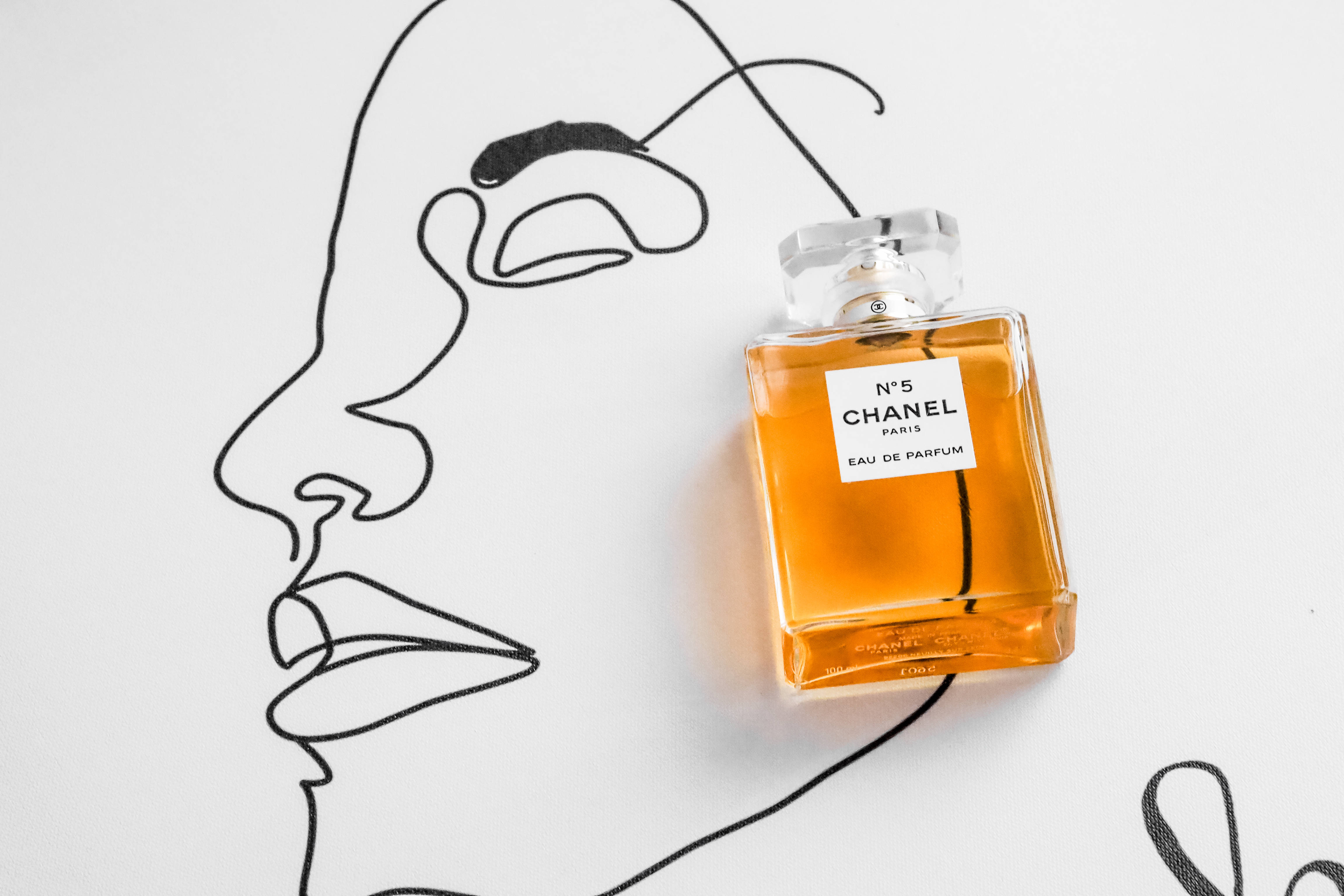 Chanel 桌布 壁紙 — 一瓶Chanel No 5香水放在白色背景上，旁邊是一幅極簡風格的黑色線條女性側面輪廓畫。