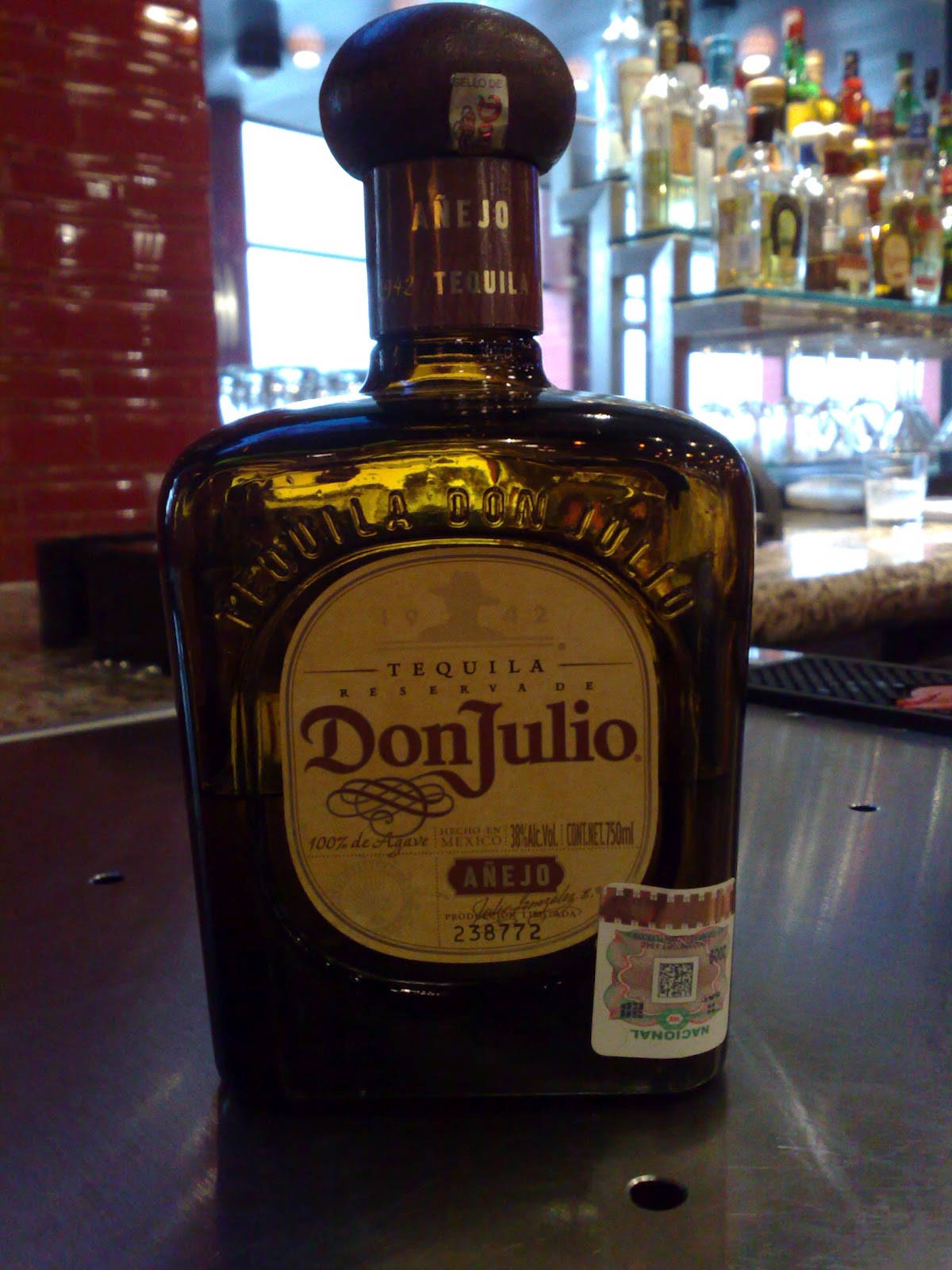 飲料 桌布 壁紙 — 一瓶Don Julio Añejo龍舌蘭酒放在吧檯上，背景有紅磚牆和酒架。