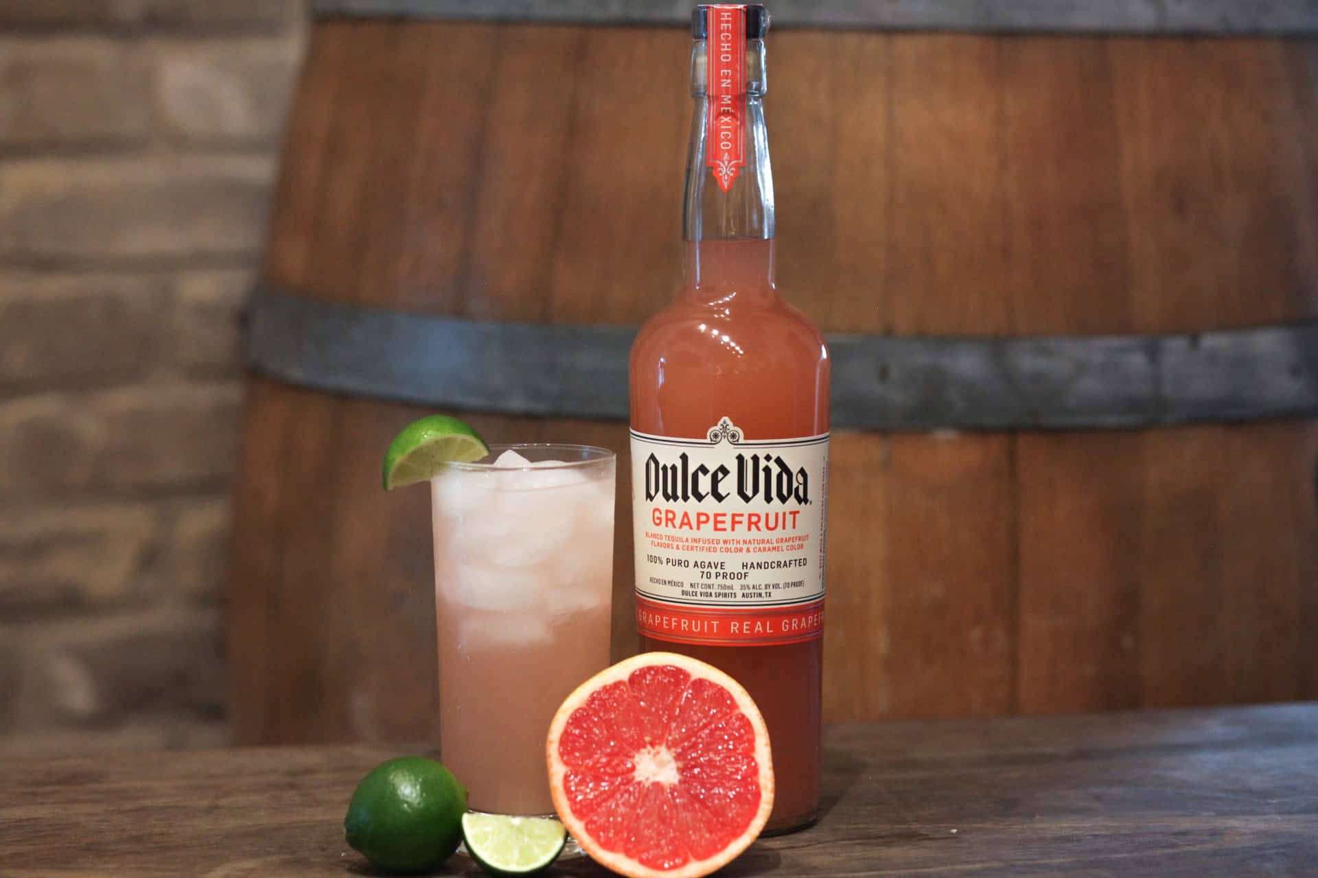 cocktail 桌布 壁紙 — 一瓶Dulce Vida葡萄柚龍舌蘭酒放在木桌上，旁邊是一杯冰涼的雞尾酒，飾以萊姆和一片葡萄柚。
