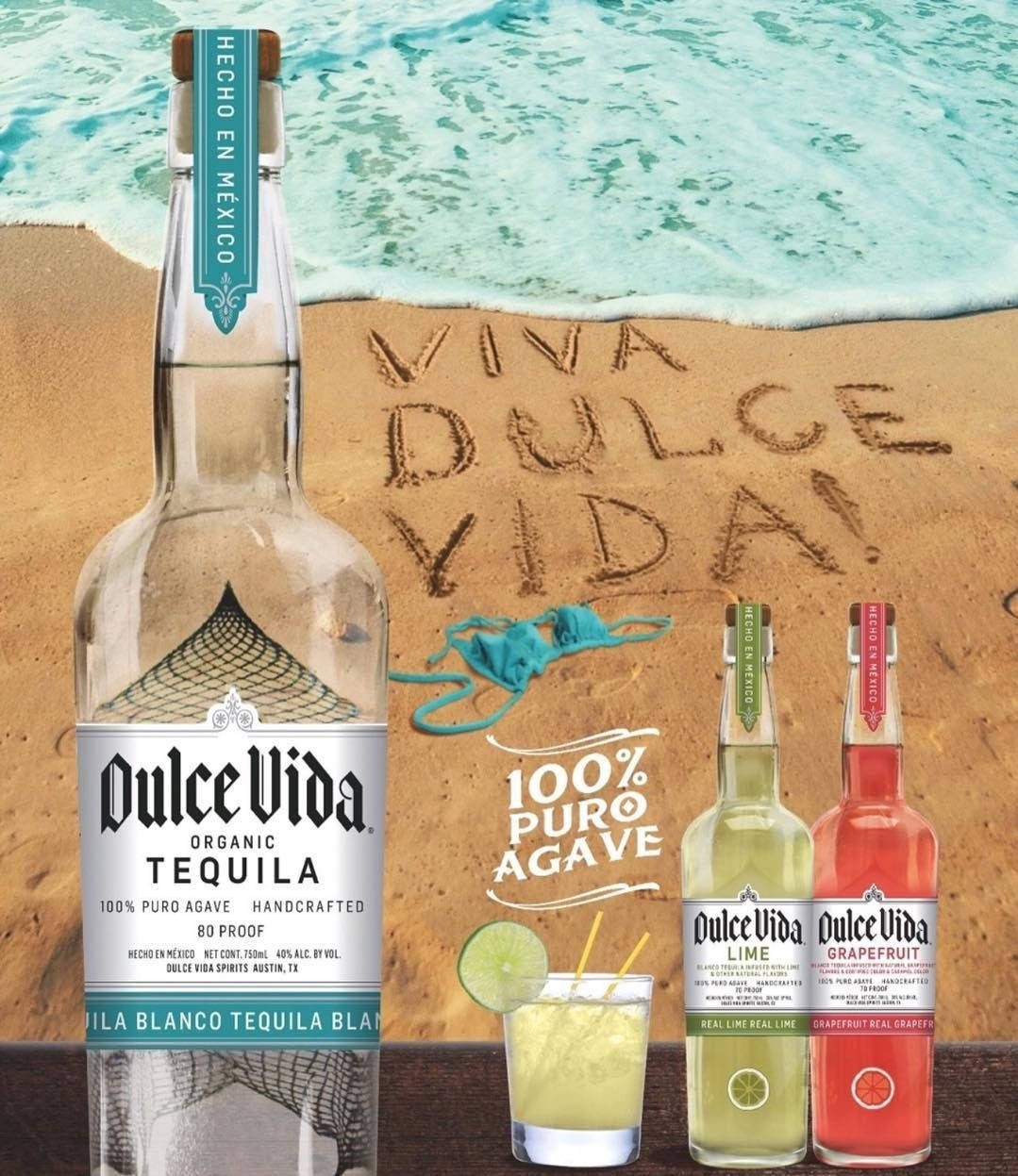 cocktail 桌布 壁紙 — 一瓶Dulce Vida龍舌蘭酒和調味烈酒放在沙灘上，旁邊的沙子上寫著「VIVA DULCE VIDA」，背景是碧綠的海浪。