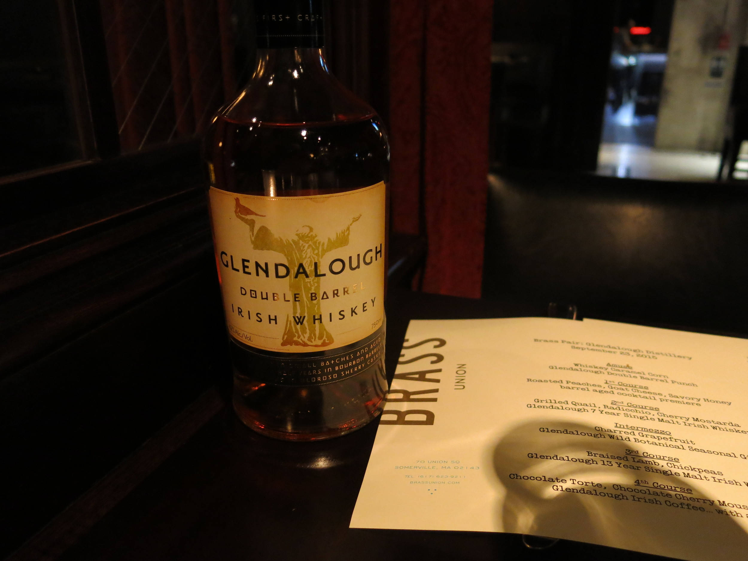 Whiskey 桌布 壁紙 — 一瓶Glendalough Double Barrel愛爾蘭威士忌放在昏暗酒吧的深色木桌上，旁邊有一份菜單。