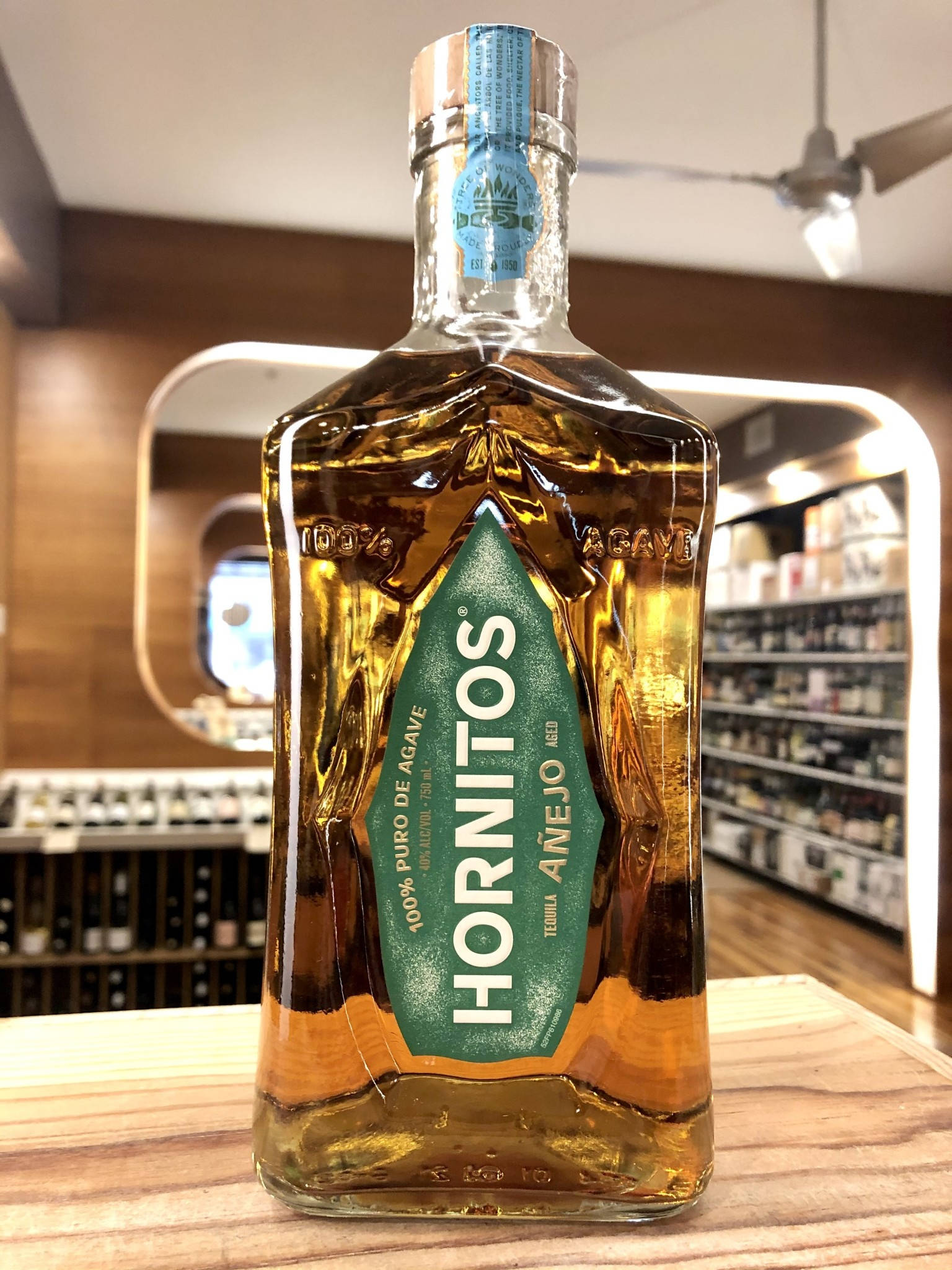 alcohol 桌布 壁紙 — 一瓶Hornitos Añejo龍舌蘭酒在光線充足的酒舖木質櫃檯上閃爍著琥珀色液體。