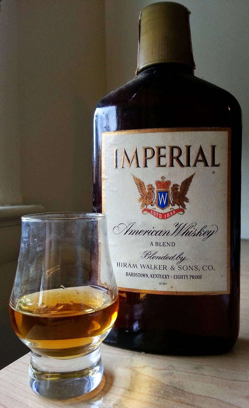 alcohol 桌布 壁紙 — 一瓶Imperial American Whiskey和一杯琥珀色液體放在木質表面上，室內光線柔和。