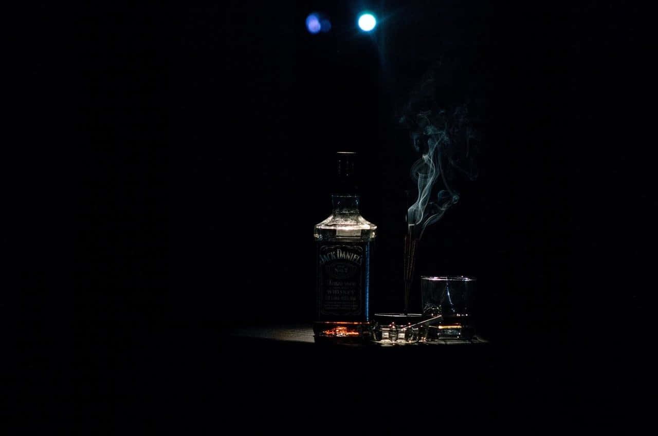 背景 桌布 壁紙 — 一瓶Jack Daniel's和玻璃杯在戲劇性的聚光燈下閃耀，煙霧在黑暗虛空中向上盤旋。