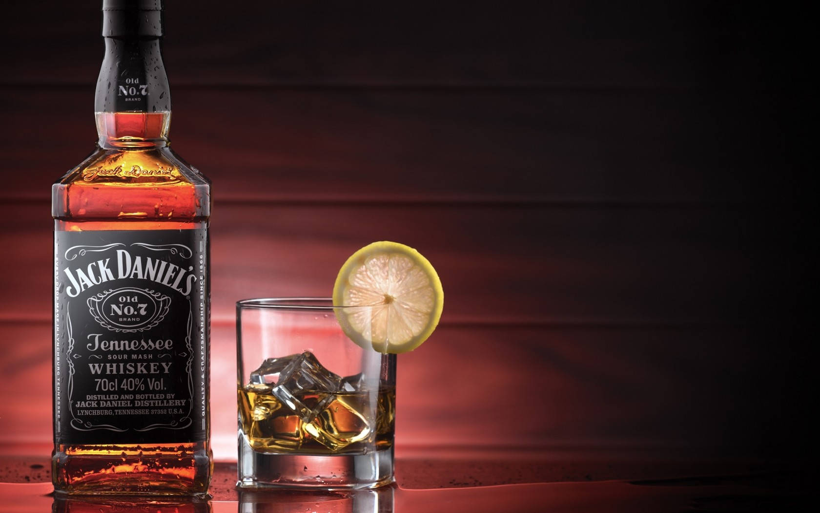 飲料 桌布 壁紙 — 一瓶Jack Daniel's威士忌和一杯加冰和檸檬片的玻璃杯在溫暖的紅色燈光下閃耀。