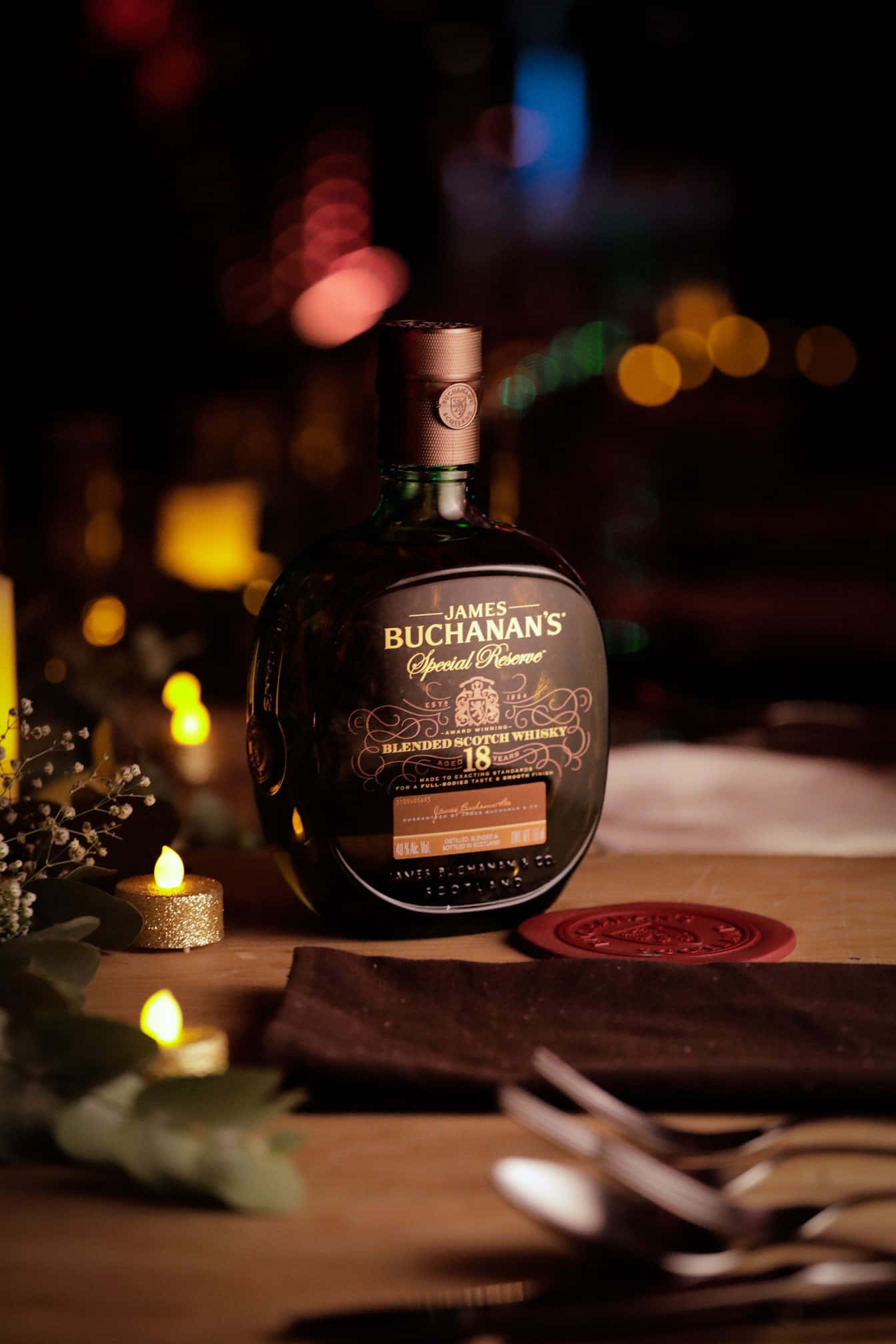 alcohol 桌布 壁紙 — 一瓶James Buchanan's Special Reserve威士忌在木桌上溫暖地發光，旁邊有閃爍的蠟燭和節日綠植。