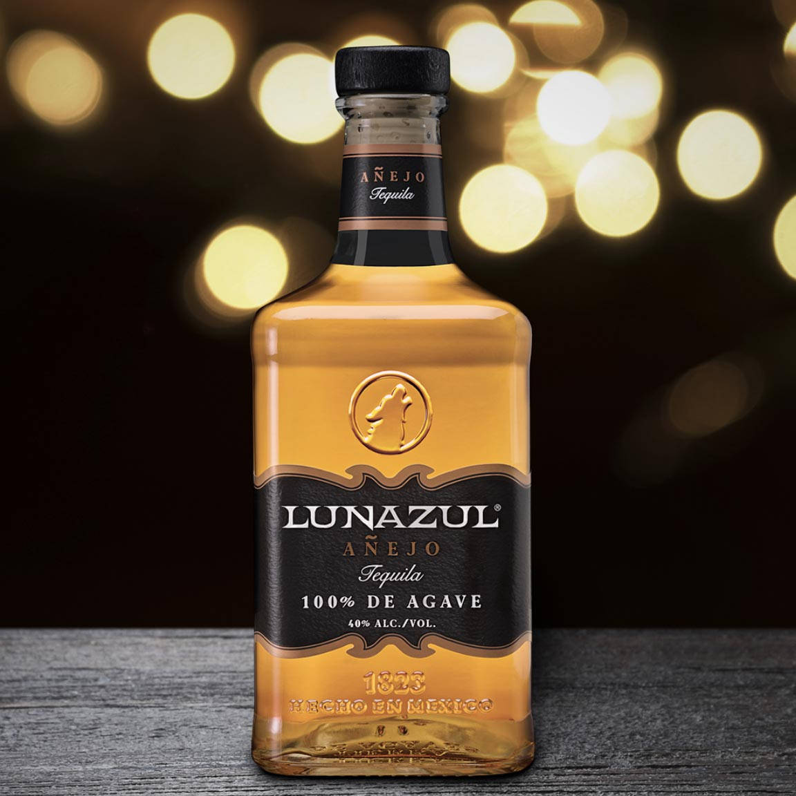 alcohol 桌布 壁紙 — 一瓶Lunazul Añejo龍舌蘭酒在木質表面上閃耀，背景是溫暖的金色散景燈光。