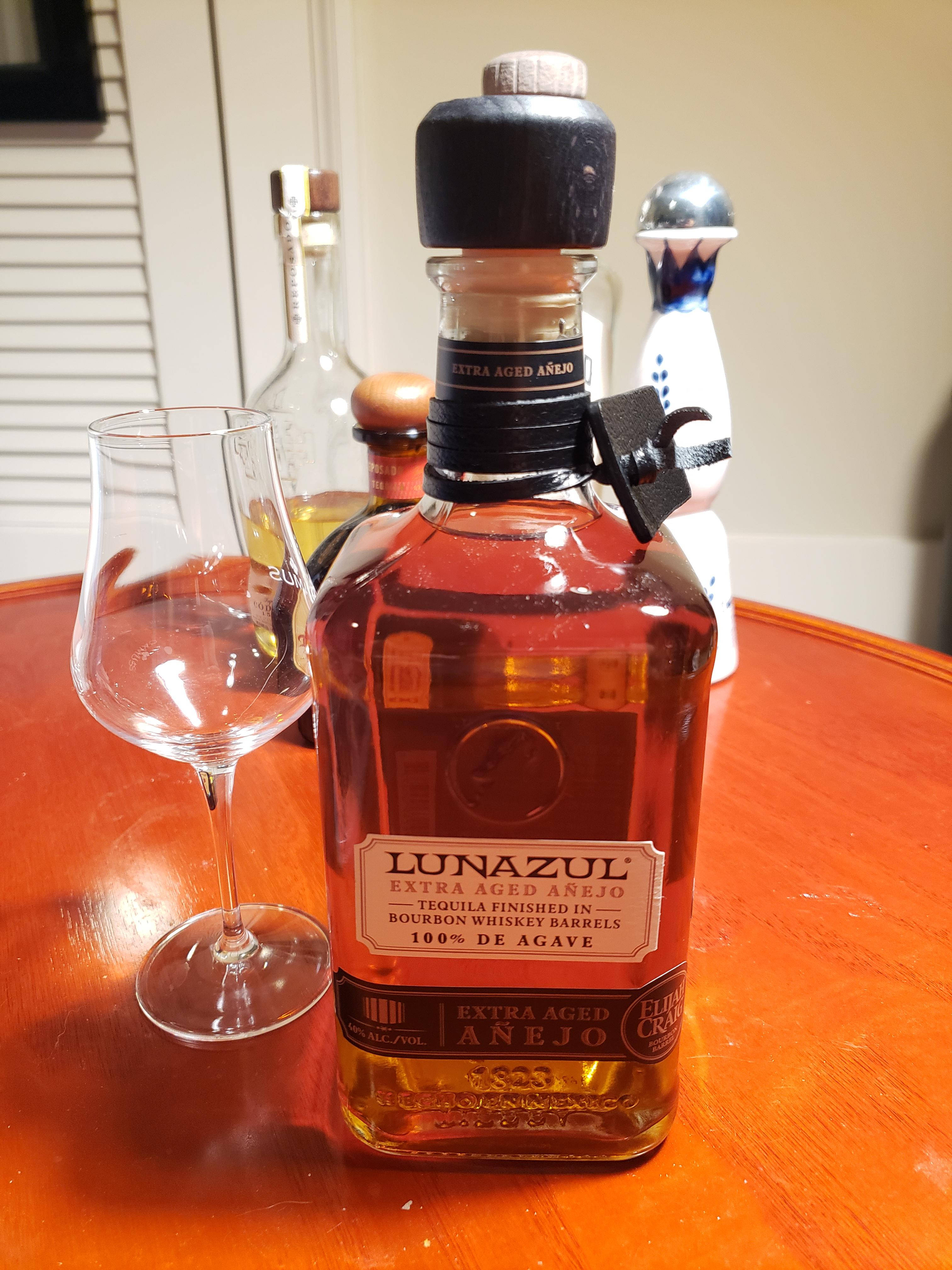 alcohol 桌布 壁紙 — 一瓶Lunazul Extra Aged Añejo龍舌蘭酒放在溫暖的木桌上，旁邊有一個空的品酒杯。