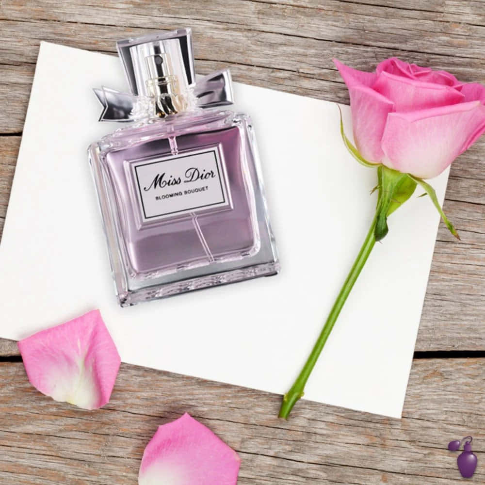 Dior 動態 桌布 壁紙 — 一瓶Miss Dior香水，配以粉紅玫瑰和花瓣，優雅地放在白色卡片上，置於風化木上。