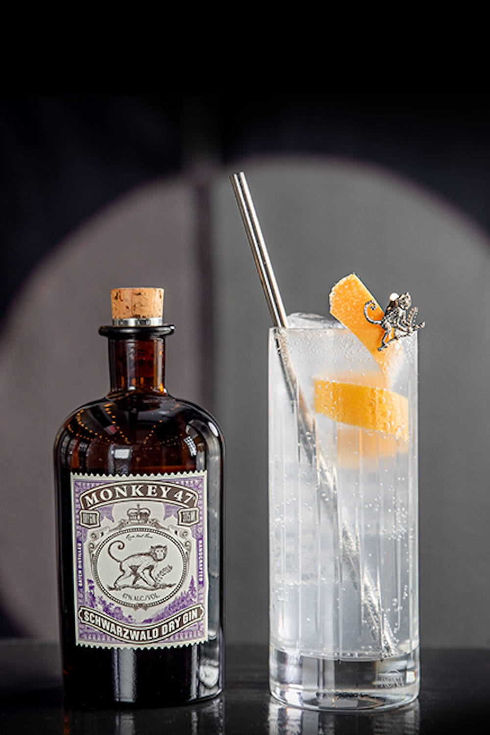 cocktail 桌布 壁紙 — 一瓶Monkey 47琴酒放在一杯高身琴酒通寧水旁邊，飾以柳橙片和猴子形攪拌棒。