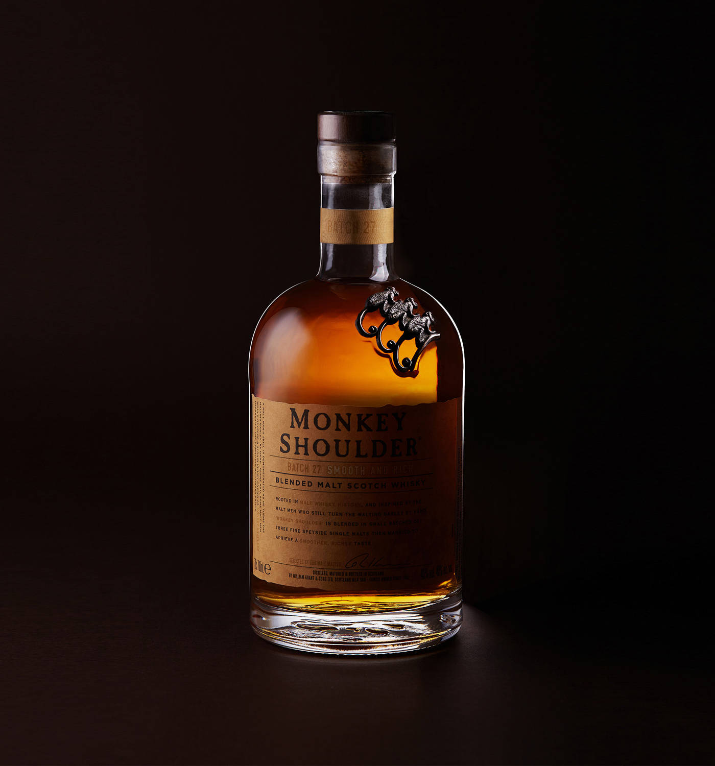 飲料 桌布 壁紙 — 一瓶Monkey Shoulder威士忌在深黑色背景上以戲劇性燈光溫暖地發光。