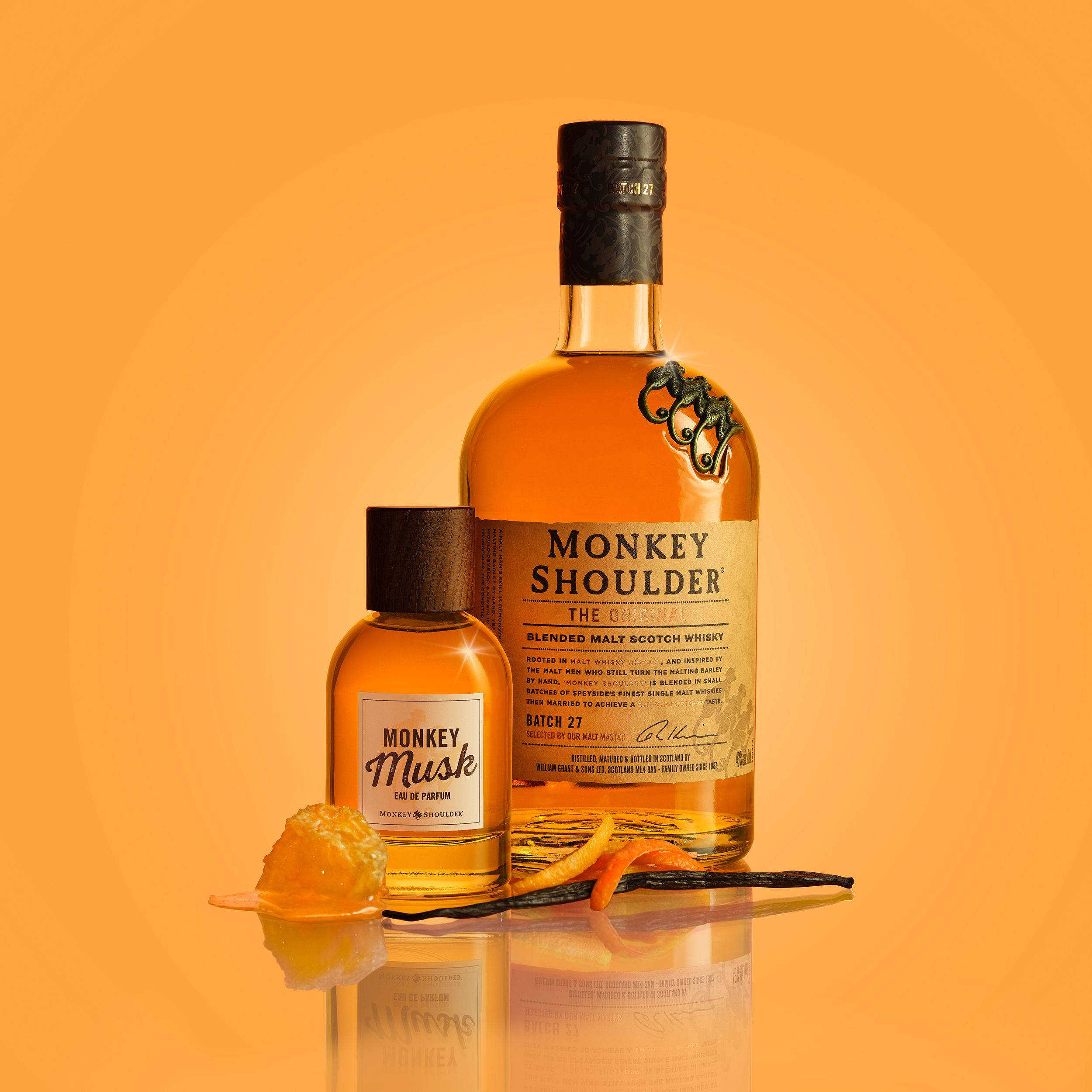 bottle 桌布 壁紙 — 一瓶Monkey Shoulder威士忌和Monkey Musk香水放在一個反光的橙色表面上，旁邊有香草豆和柑橘皮。