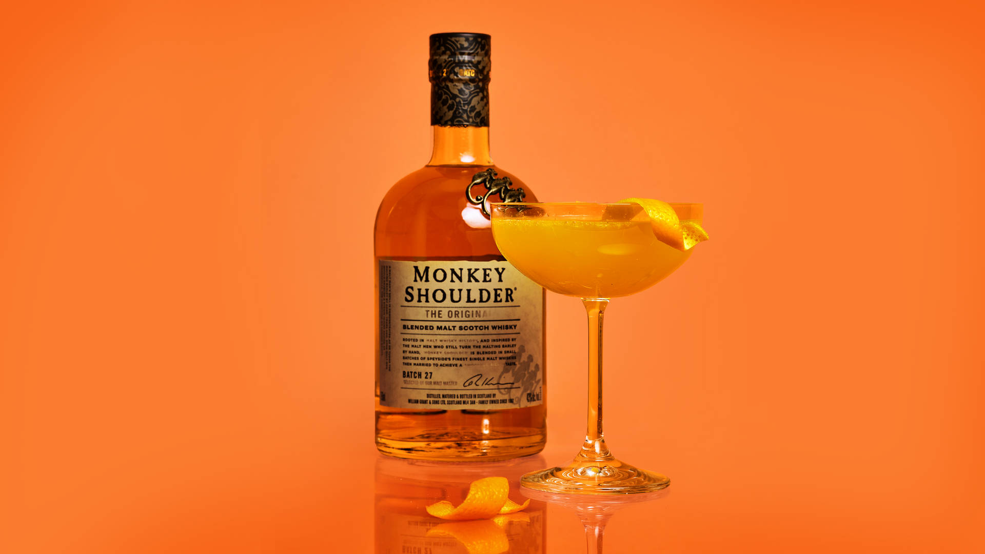 alcohol 桌布 壁紙 — 一瓶Monkey Shoulder威士忌和柑橘雞尾酒在帶有反光表面的鮮豔橙色背景下閃耀。