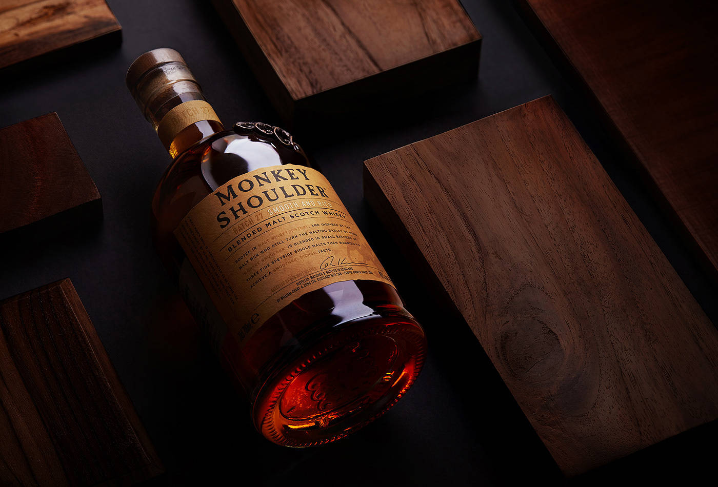 alcohol 桌布 壁紙 — 一瓶Monkey Shoulder威士忌在戲劇性燈光下斜放在深色木塊上。