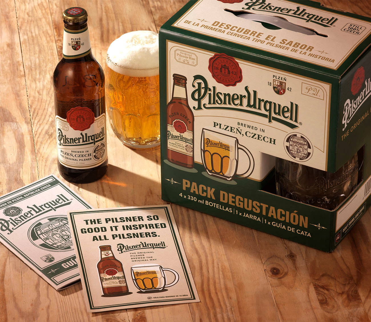booze 桌布 壁紙 — 一瓶Pilsner Urquell啤酒、玻璃杯和品嚐套裝放在一張溫暖的木桌上，沐浴在金色的陽光中。