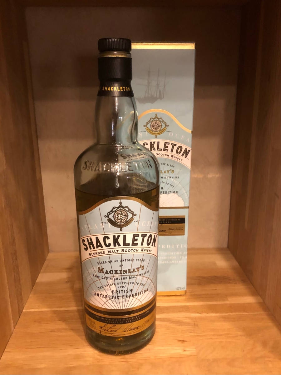 飲料 桌布 壁紙 — 一瓶Shackleton Blended Malt Scotch Whisky放在木架上，旁邊是其盒子，燈光溫暖。