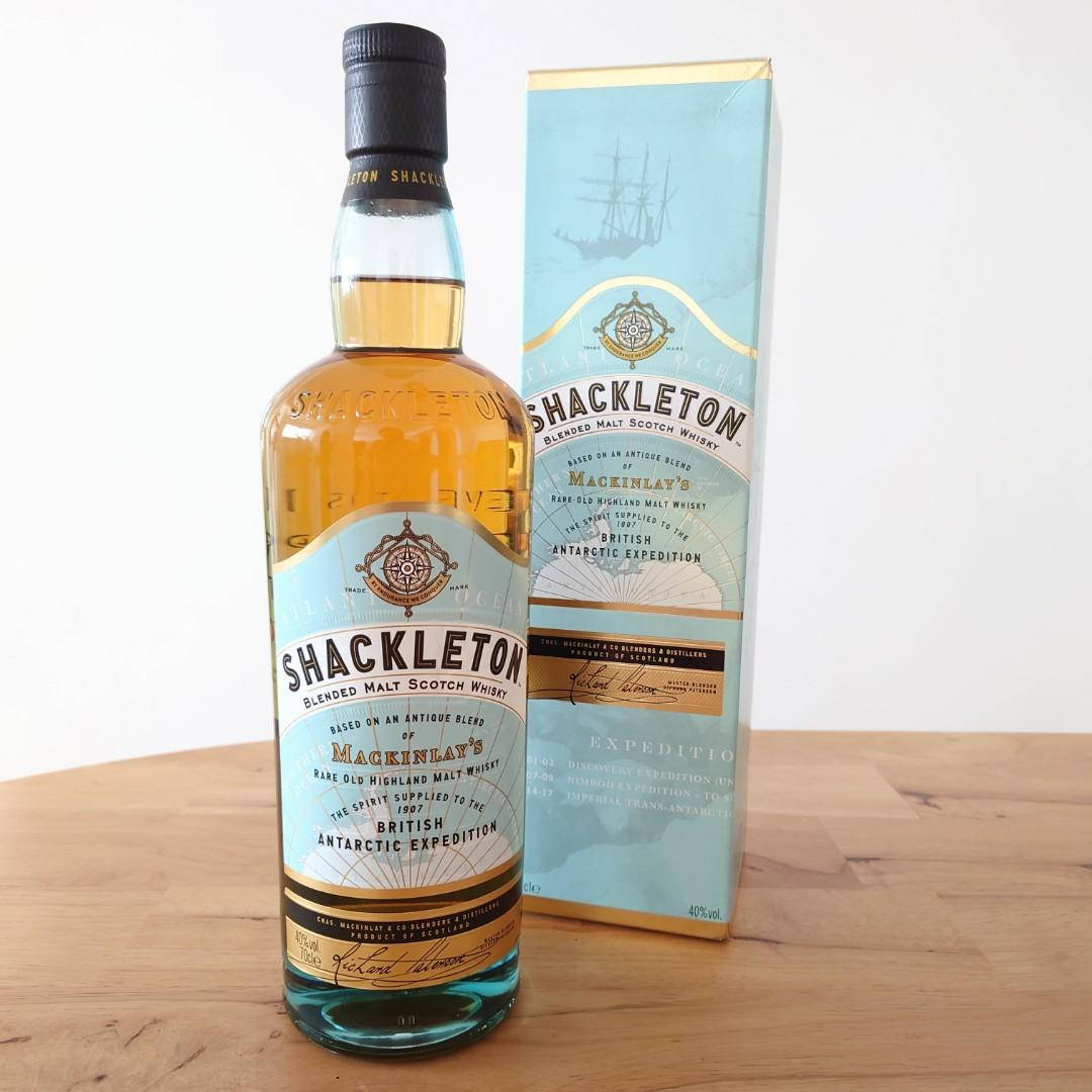 Drink 桌布 壁紙 — 一瓶Shackleton Blended Malt Scotch Whisky連同其包裝盒，放在淺色木桌上，背景為純白色。