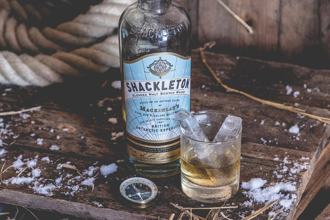 Drink 桌布 壁紙 — 一瓶Shackleton威士忌和一杯加冰的威士忌放在一張積雪的木桌上，旁邊有一個指南針和一條繩子。