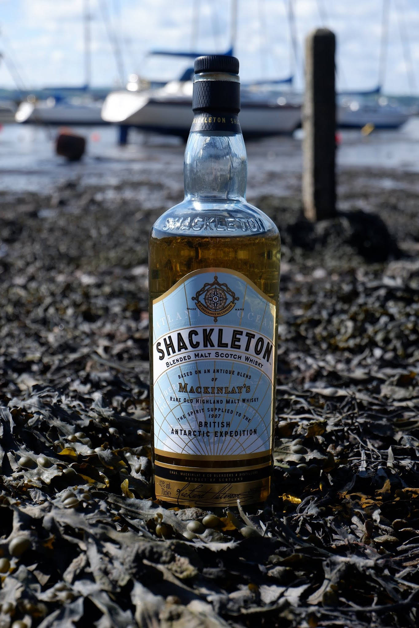 Drink 桌布 壁紙 — 一瓶Shackleton威士忌直立在海藻床上，背景有模糊的帆船。
