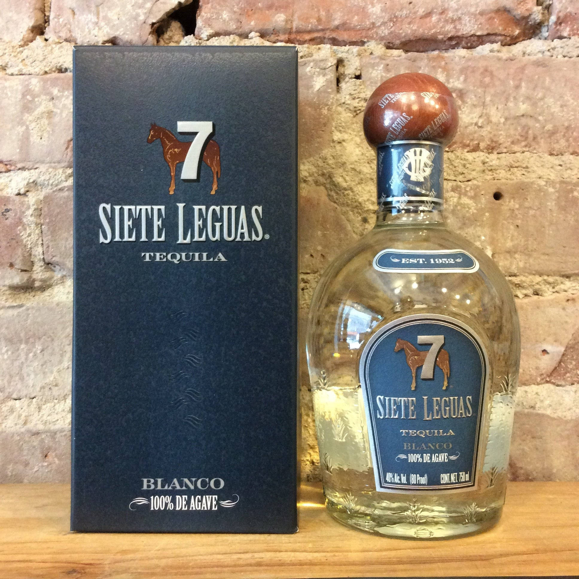 高清 桌布 壁紙 — 一瓶Siete Leguas龍舌蘭酒瓶和盒子並排放在木質表面上，背景是質樸的磚牆。