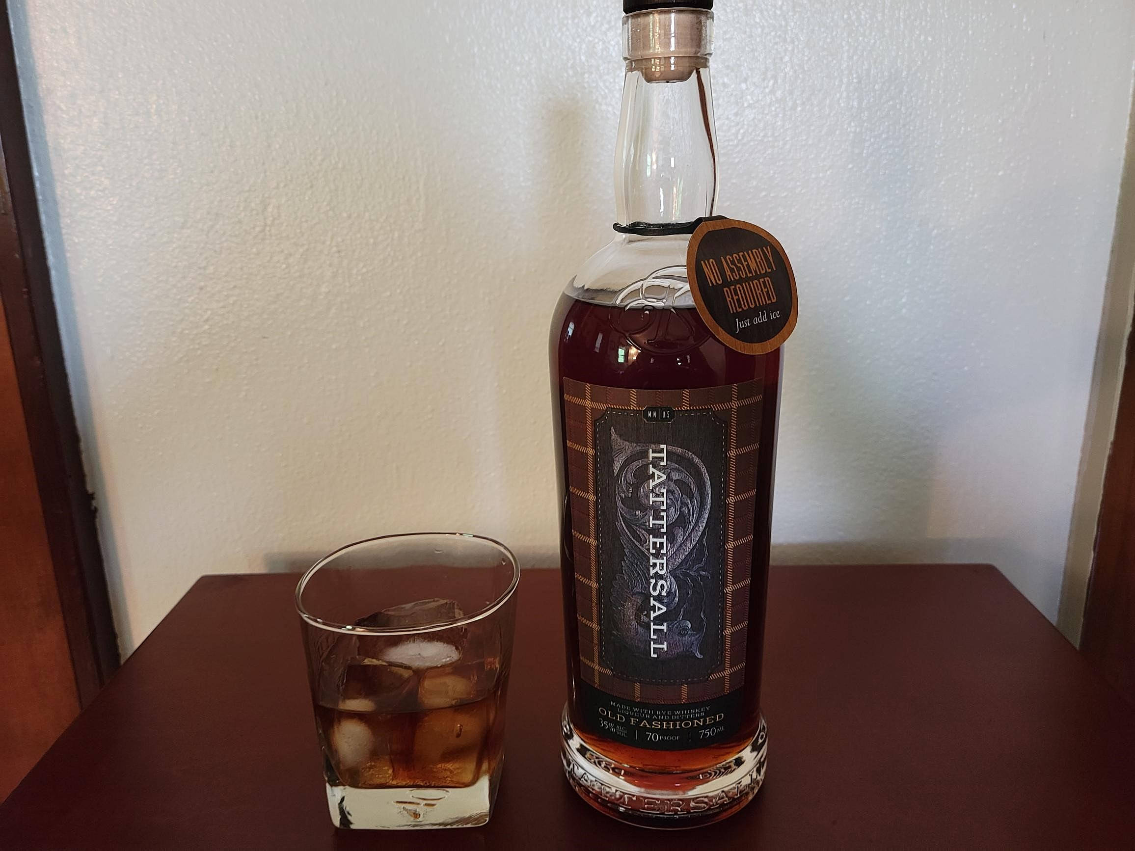 cocktail 桌布 壁紙 — 一瓶Tattersall Old Fashioned威士忌連同加冰的酒杯放在深色木桌上，背景是帶紋理的白色牆壁。