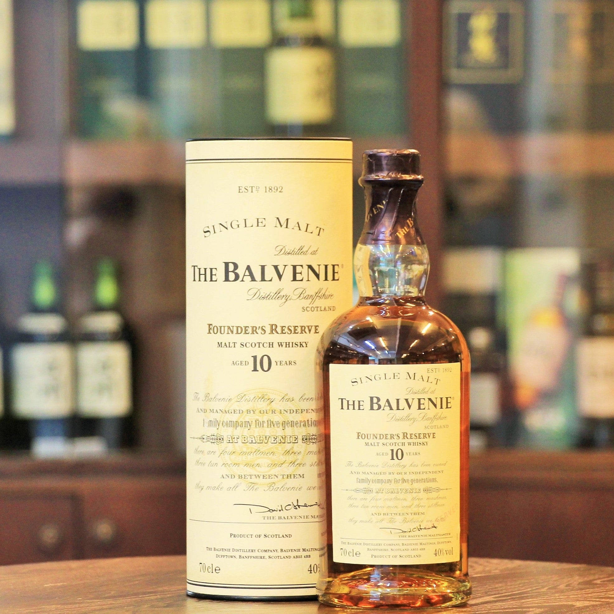 Drink 桌布 壁紙 — 一瓶The Balvenie Founder's Reserve 10年單一麥芽威士忌連同其盒子放在木製吧檯上，背景是模糊的其他酒瓶架。