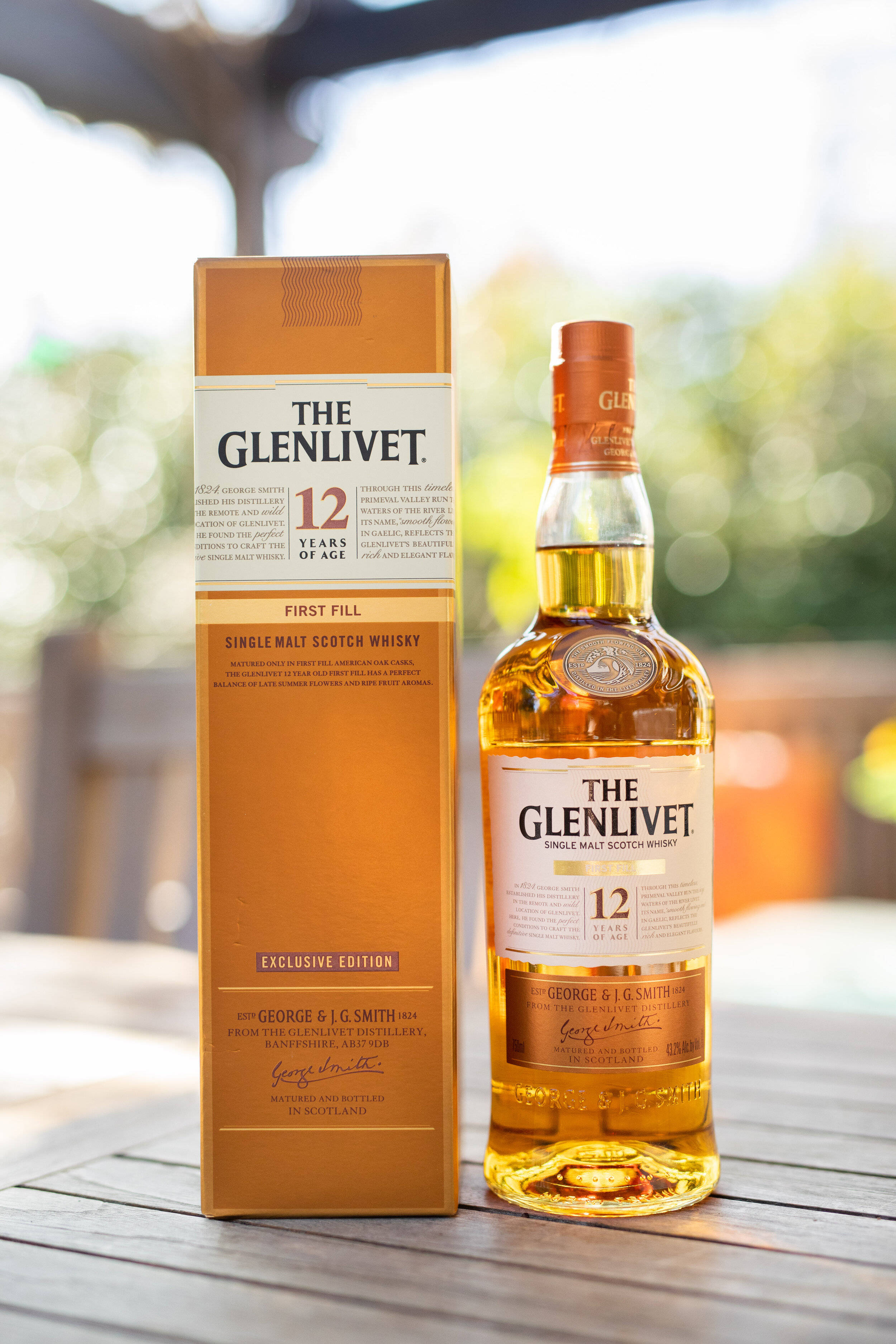 飲料 桌布 壁紙 — 一瓶The Glenlivet 12 Year Old Single Malt Scotch Whisky放在木桌上，旁邊是其盒子，在戶外柔和自然光下。